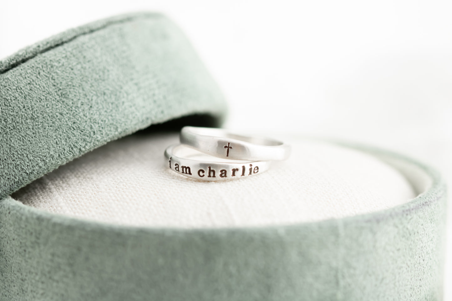 Silver ring with 'iam charlie' engraving on a light green fabric background