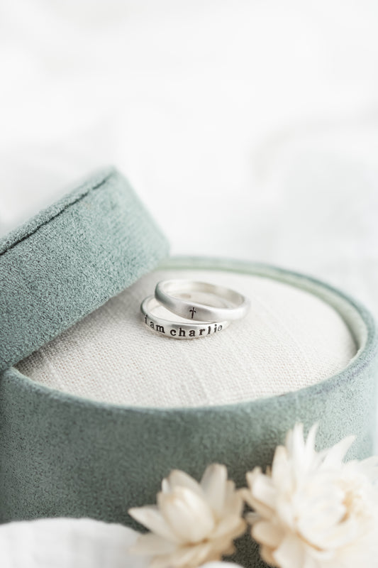 Two silver rings in a green jewelry box with white flowers on a light background