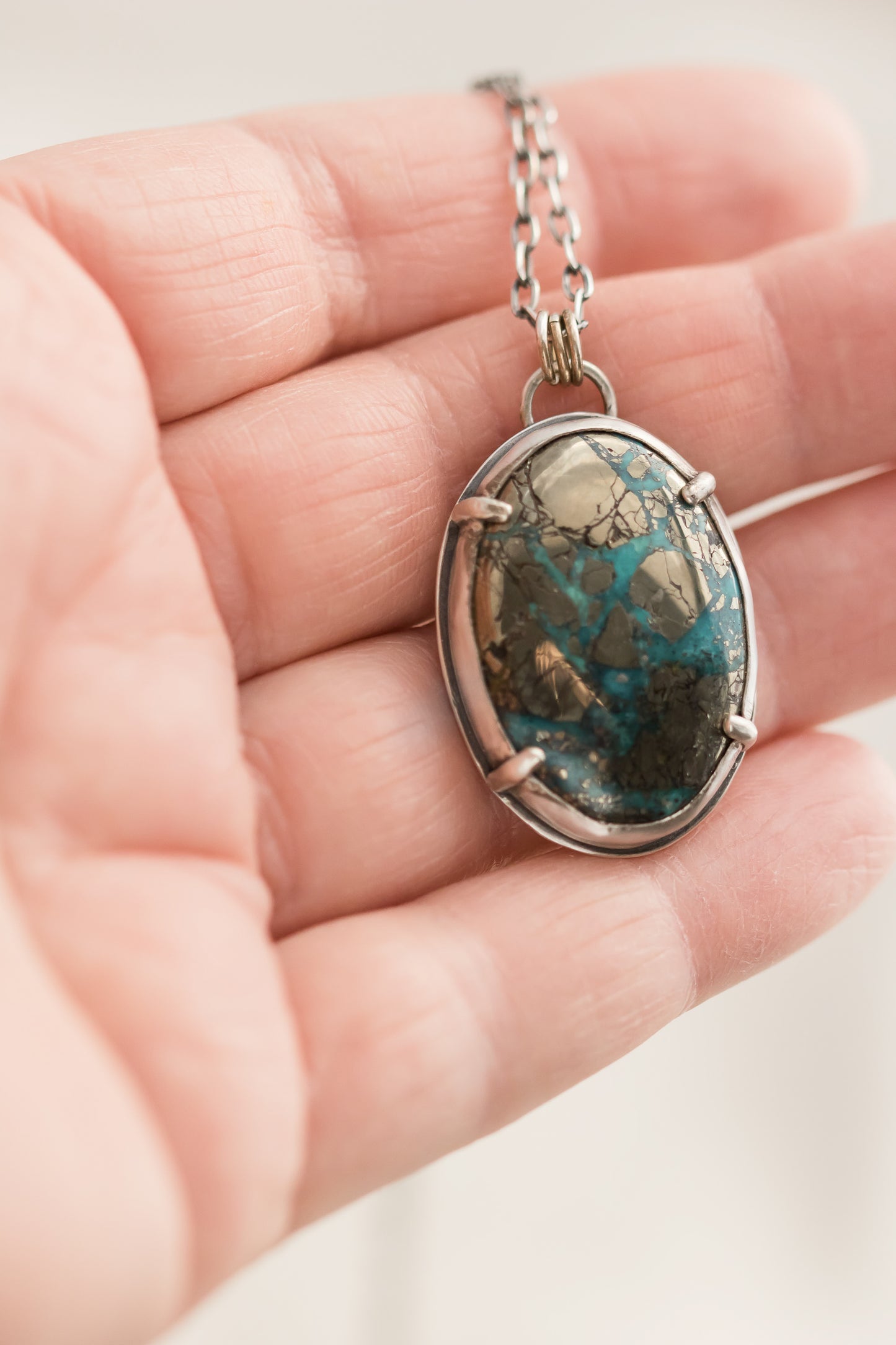 Hand holding Morenci II turquoise and pyrite necklace, close-up of stone and silver bezel