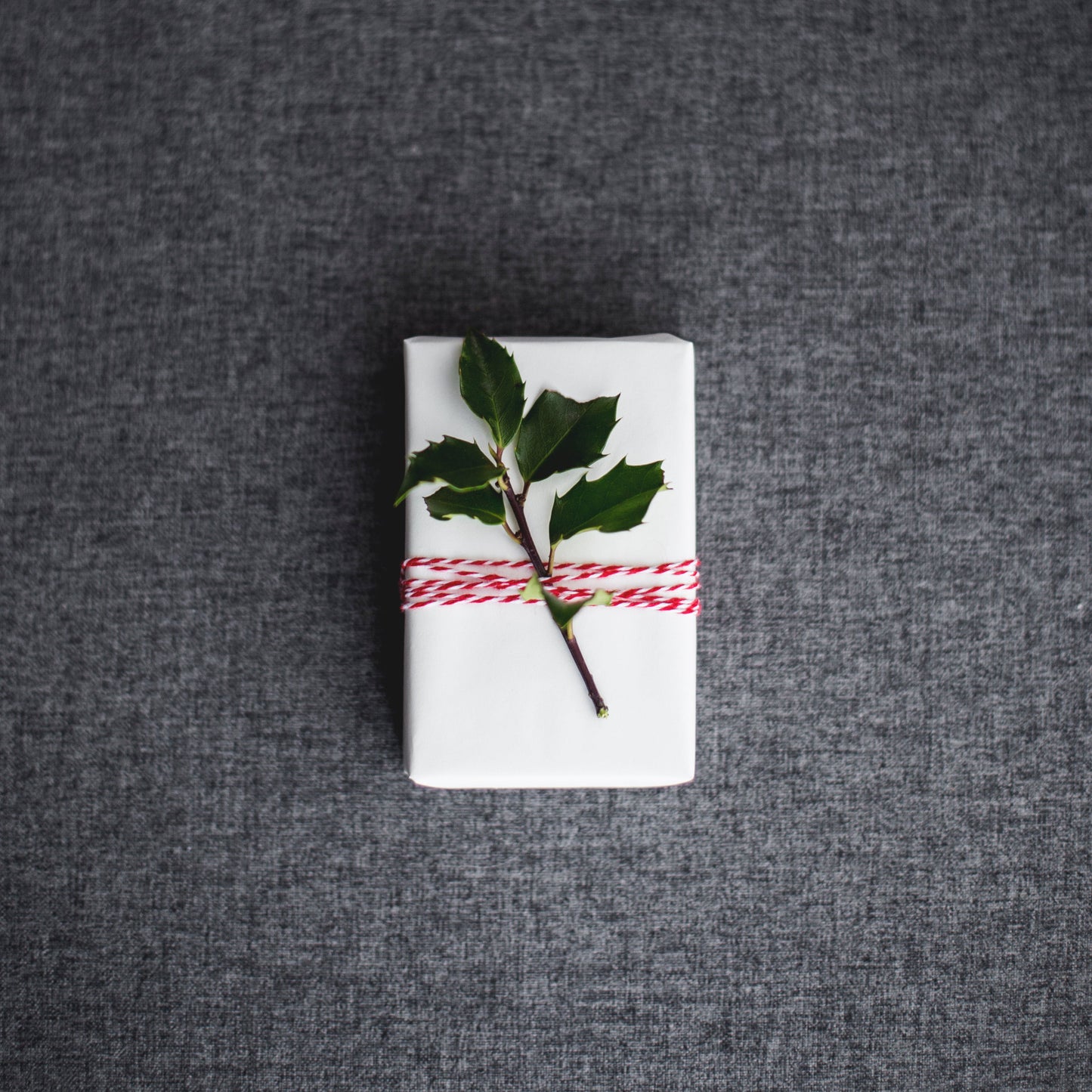 Small wrapped gift with a holly leaf on a textured gray surface