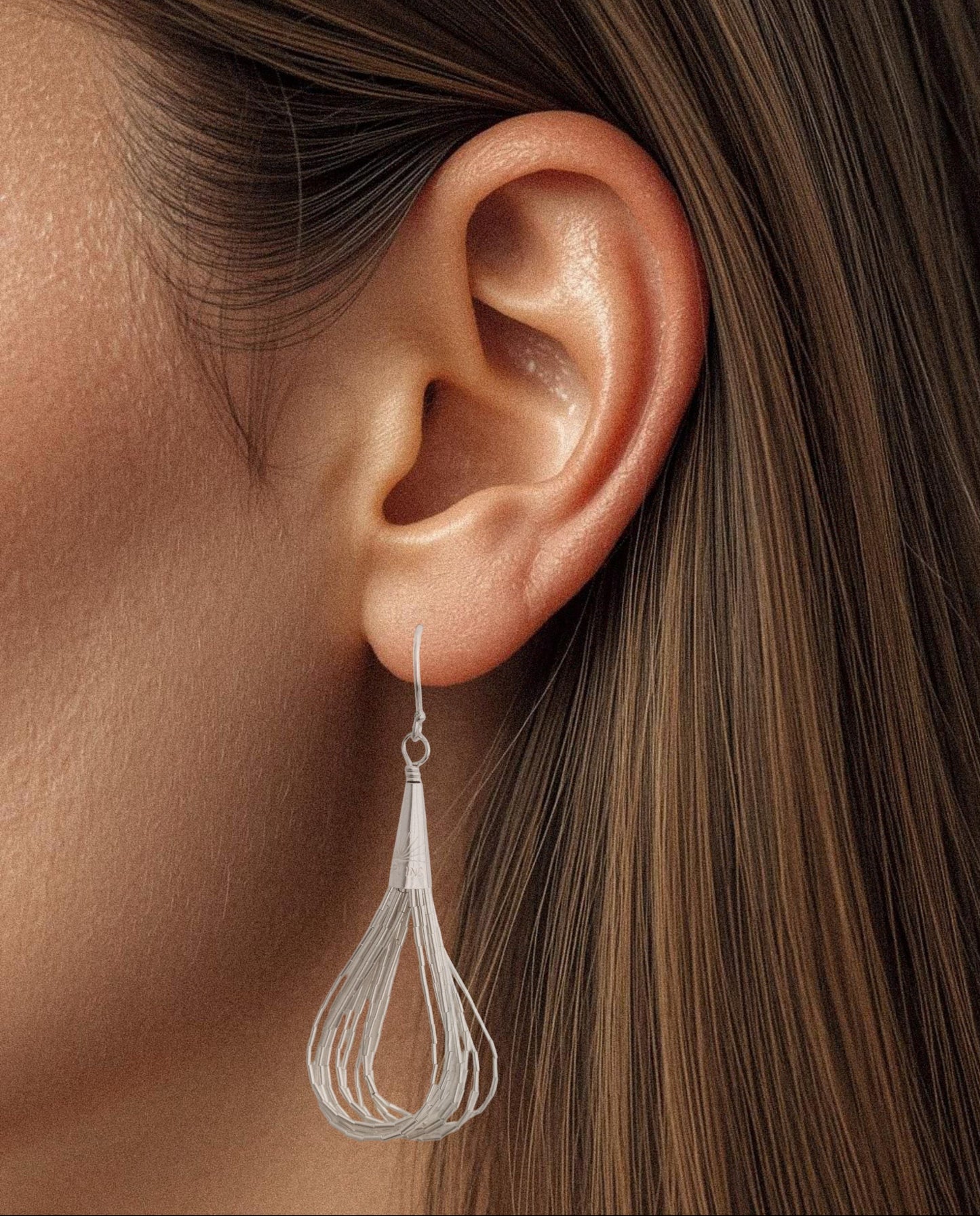 Side close-up of a model with brown hair wearing one sterling silver liquid flow earring, showing how it dangles gracefully from the ear.