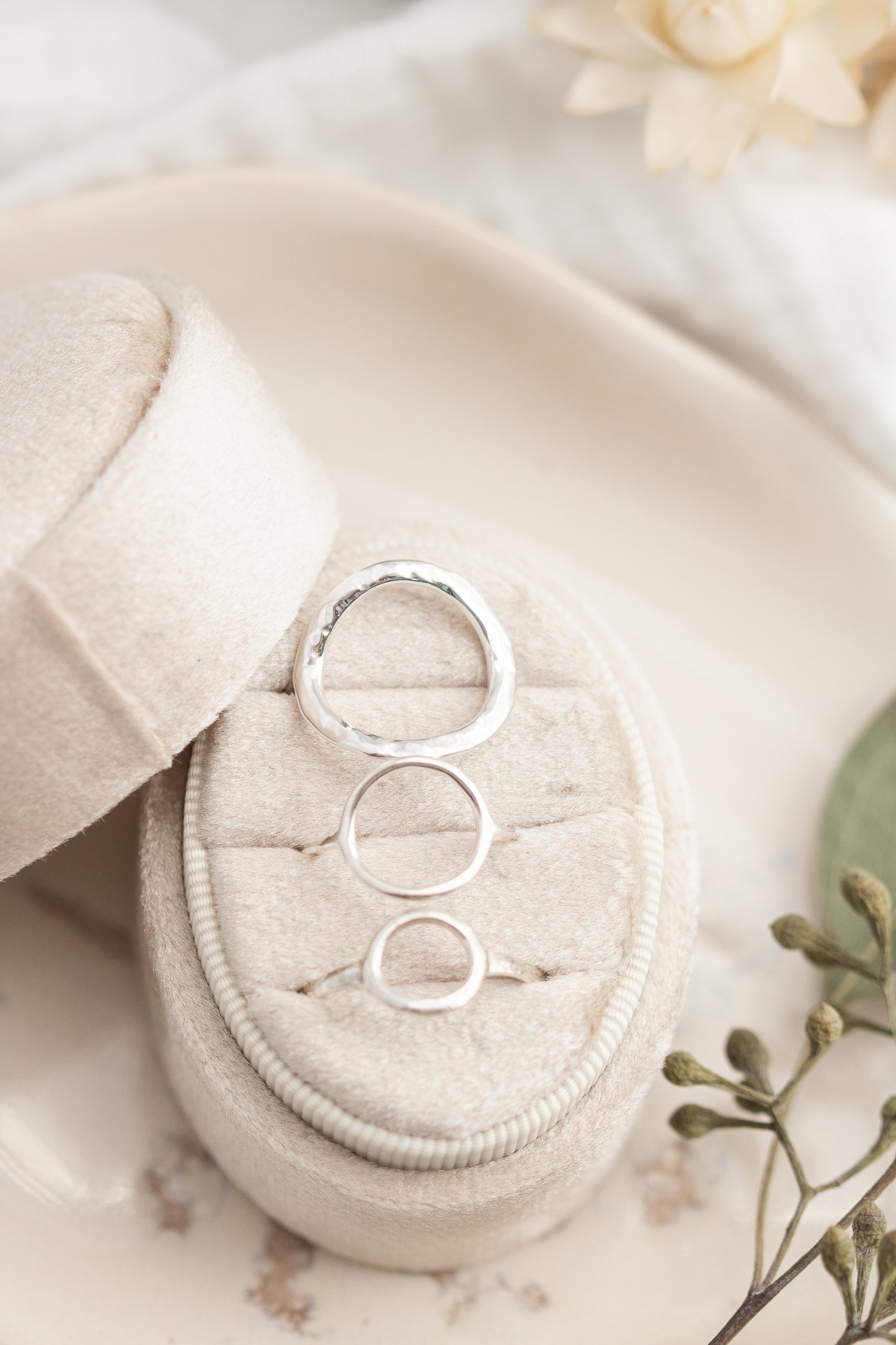 Three open circle sterling silver rings in small, medium, and large sizes, with the large ring featuring a hammered finish, elegantly displayed in a cream-colored ring box with dried leaves and flowers.