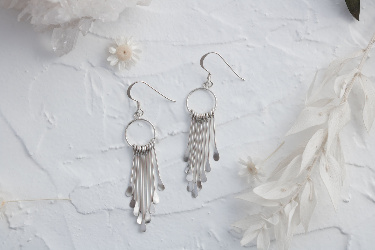 Pair of 925 sterling silver fringe dangle earrings displayed on a textured white surface with flowers and crystals.