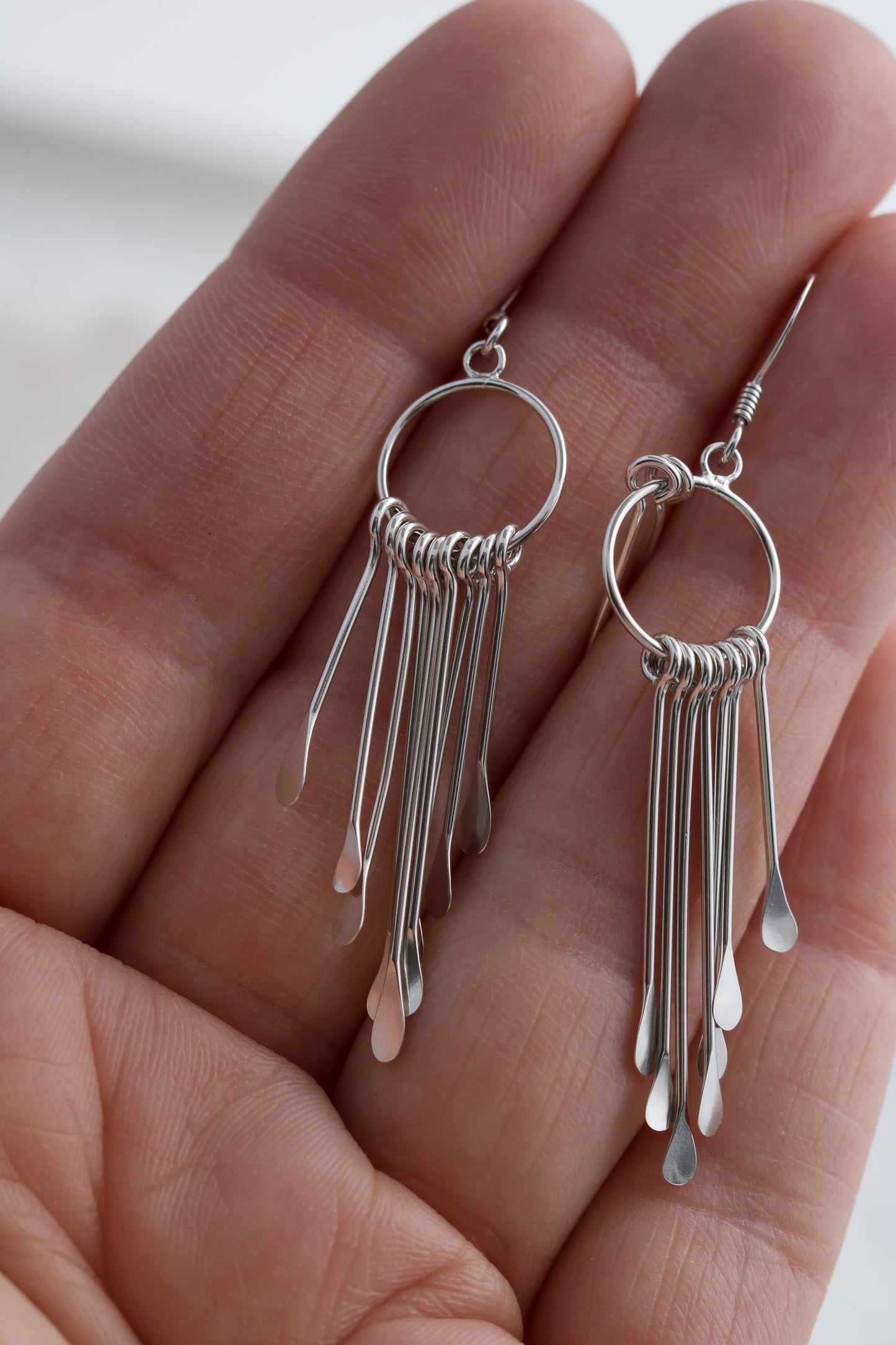 Close-up of a hand holding a pair of 925 sterling silver fringe dangle earrings with multiple dangling elements.