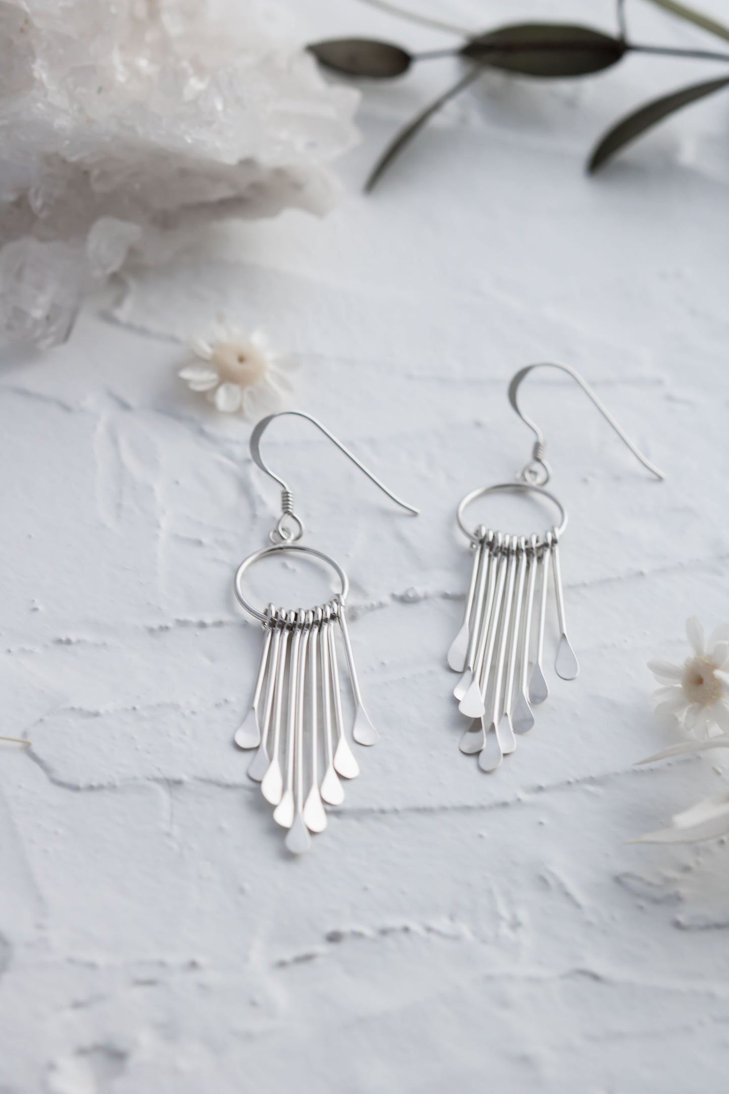 Pair of 925 sterling silver fringe dangle earrings displayed on a textured white surface with flowers and crystals.