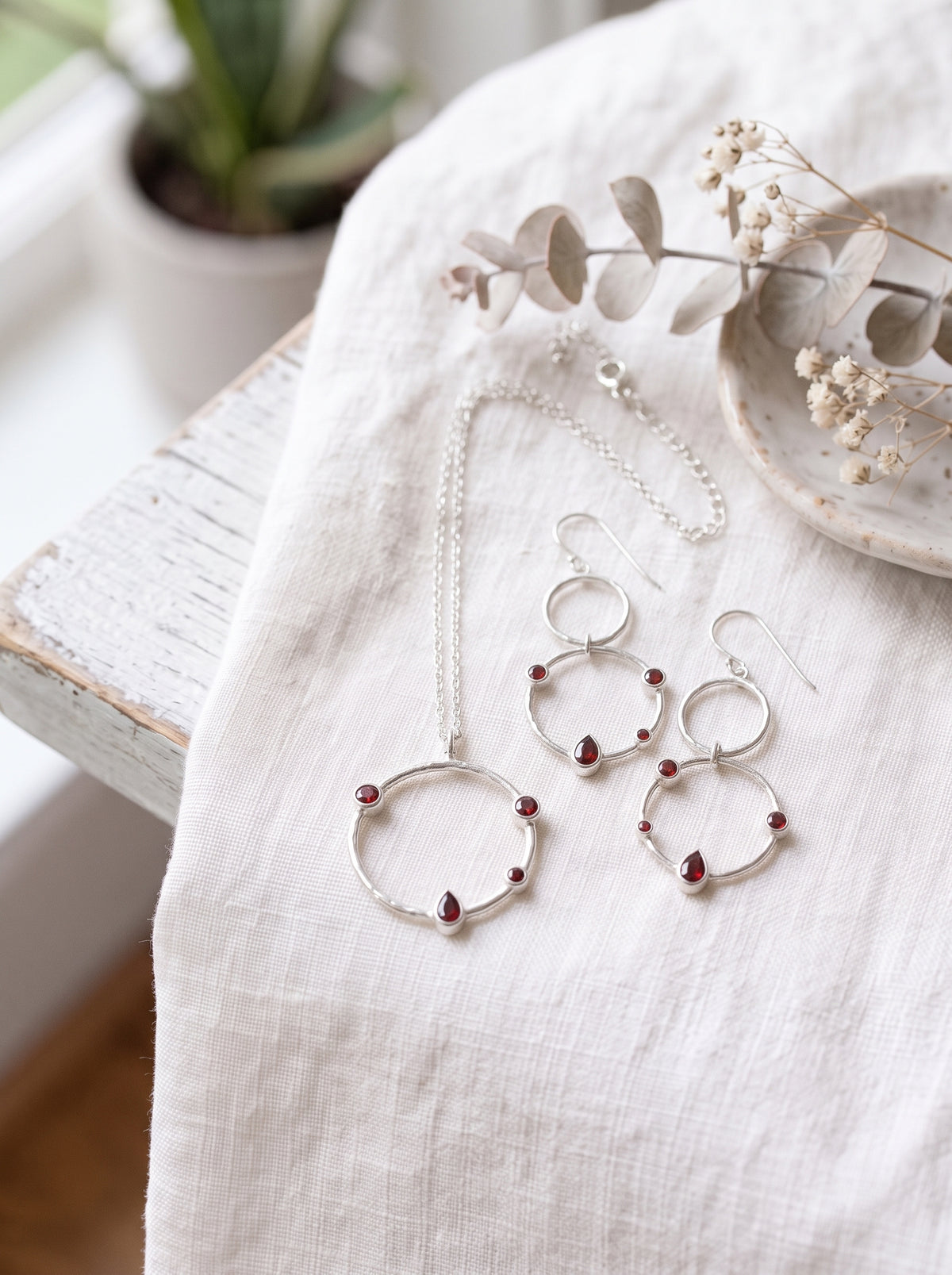 Garnet double-circle earrings beside the matching hammered-circle sterling silver necklace on cream fabric.