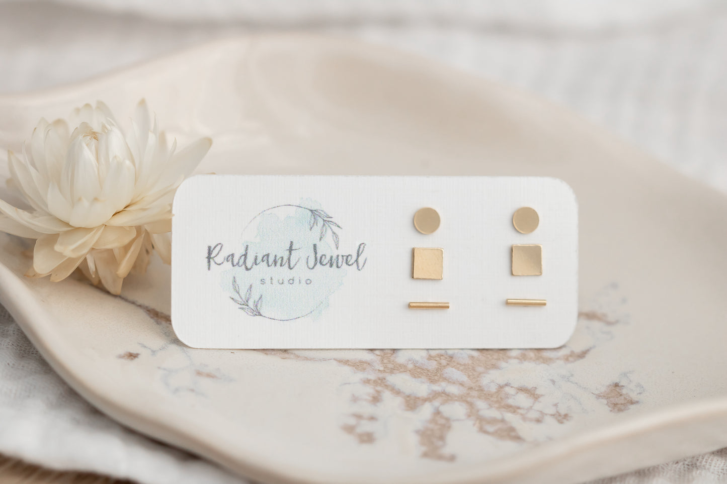 14k gold filled stud earring set displayed on ceramic dish with flower and branded card, featuring geometric stud pairs.