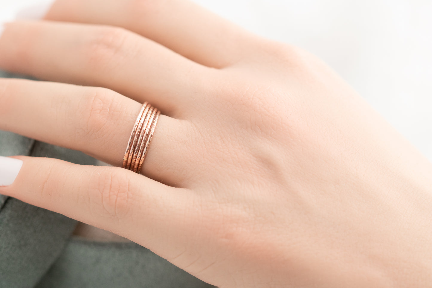 Rose gold ring on a person's finger against a neutral background