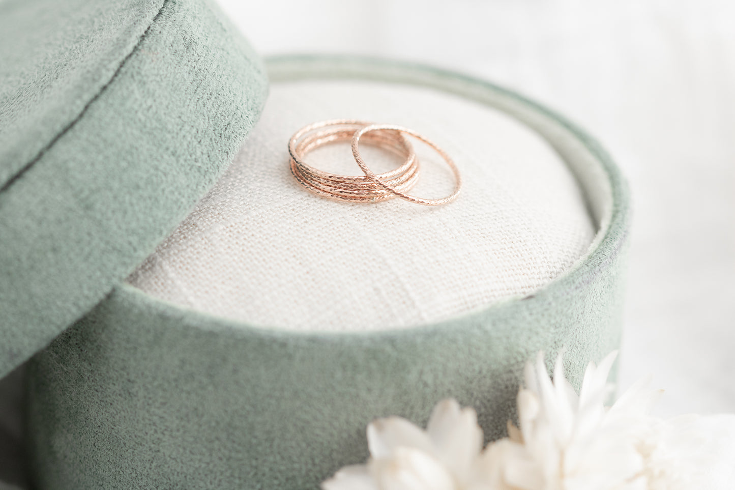 Two rose gold rings in a green jewelry box with white flowers.