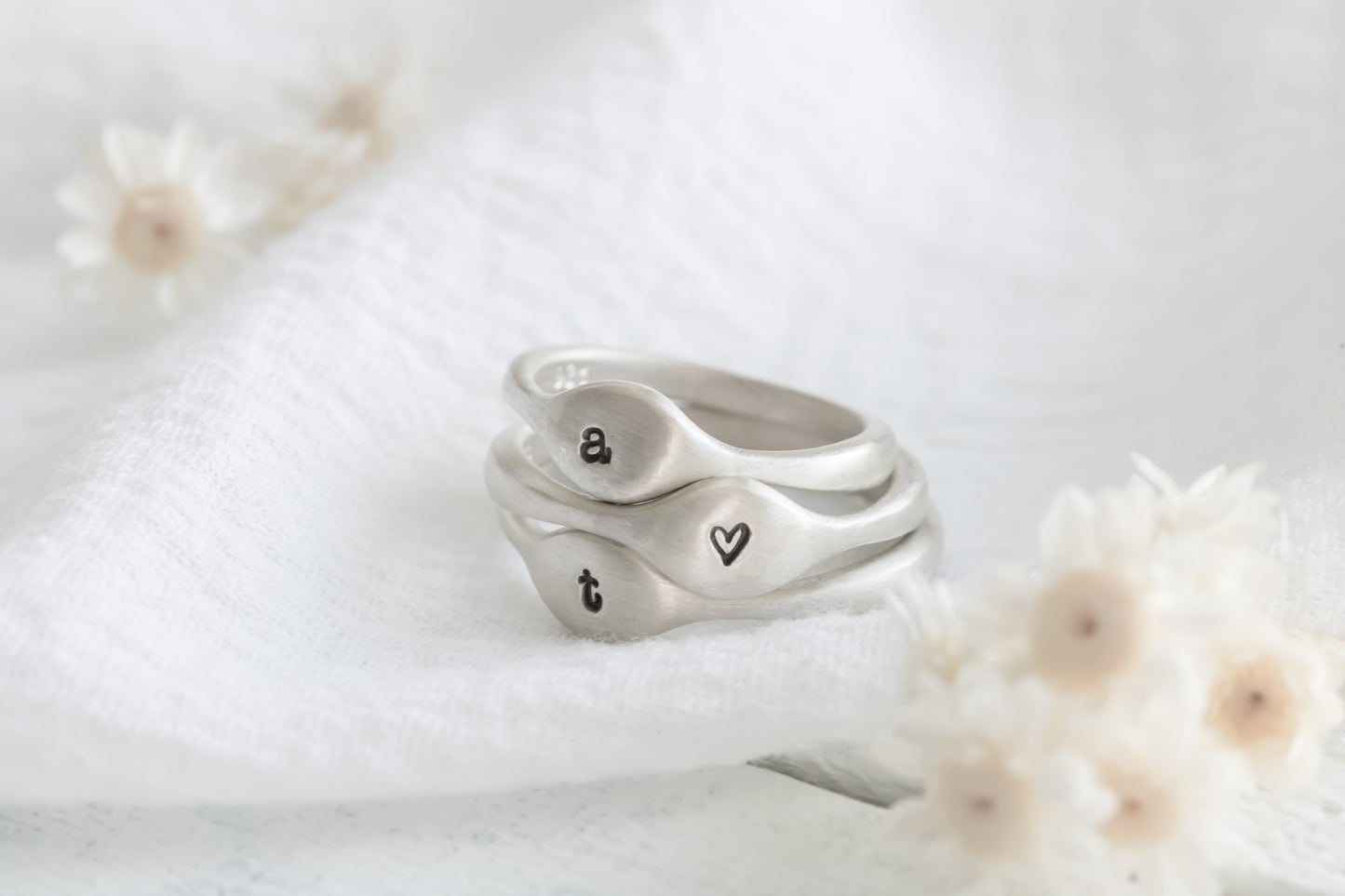 Sterling silver ring with a paw print symbol on a white textured surface with dried flowers and crystals in the background.