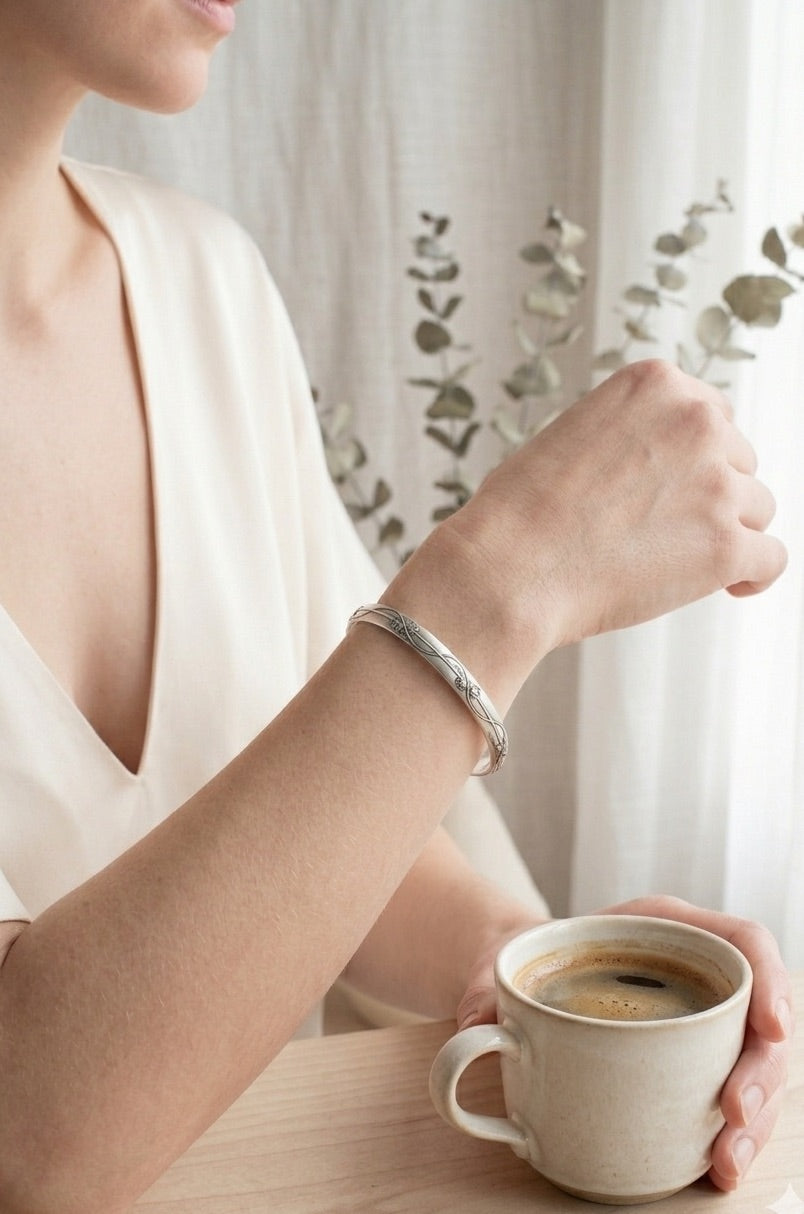Person wearing a sterling silver cuff bracelet with floral vine design, holding a cup of coffee with a blurred background