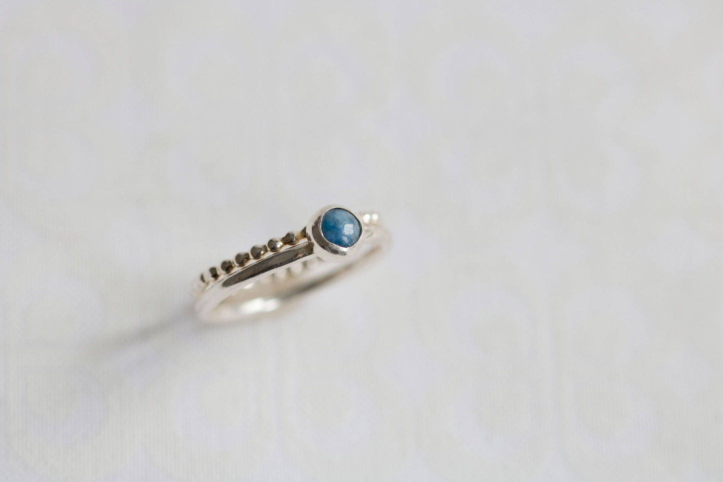 Close-up of a denim lapis ring with a beaded silver band on a white background with green leaves.