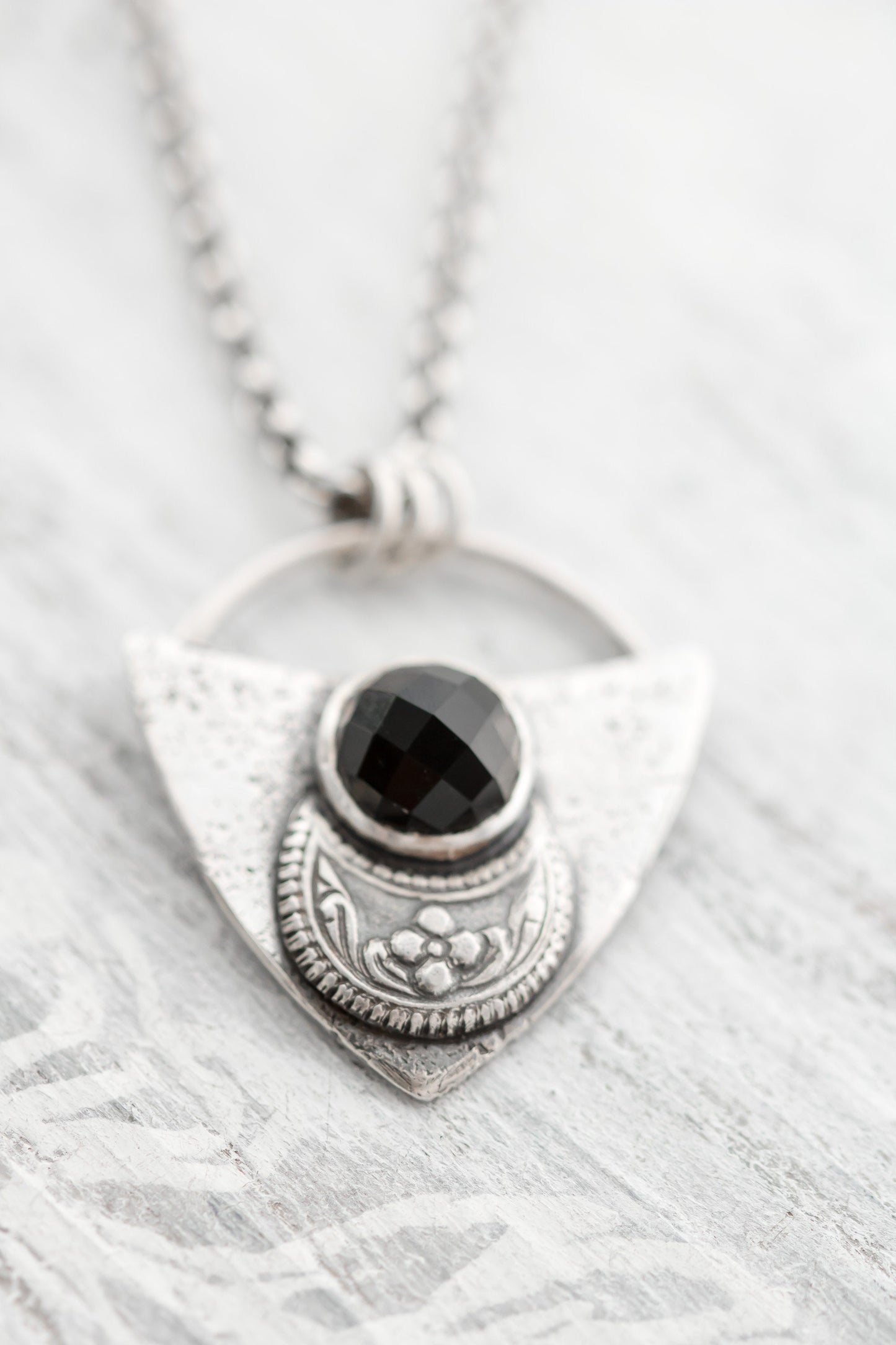 Shield shaped sterling silver pendant with floral patterned moon and faceted black onyx cabochon.