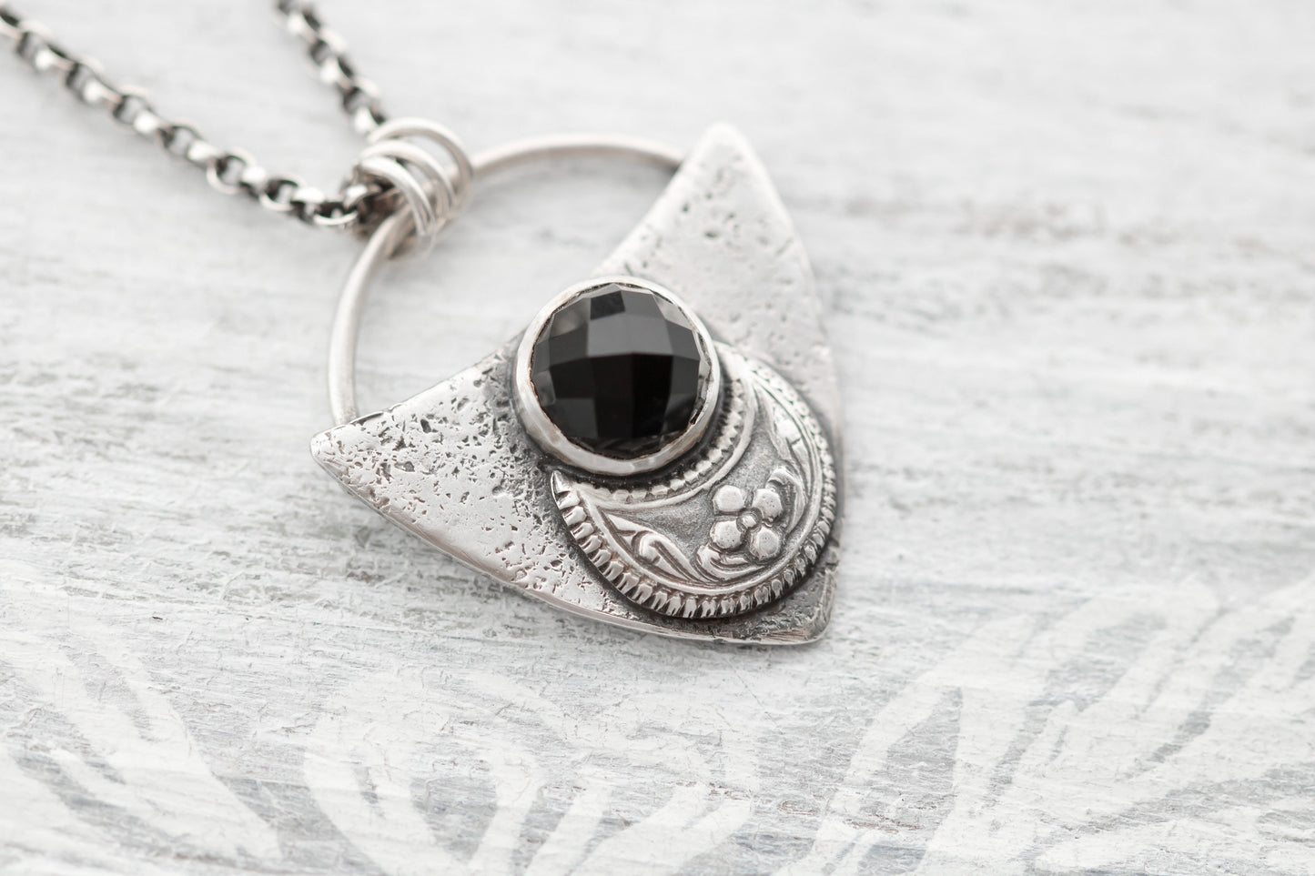 Shield shaped sterling silver pendant with floral patterned moon and faceted black onyx cabochon.