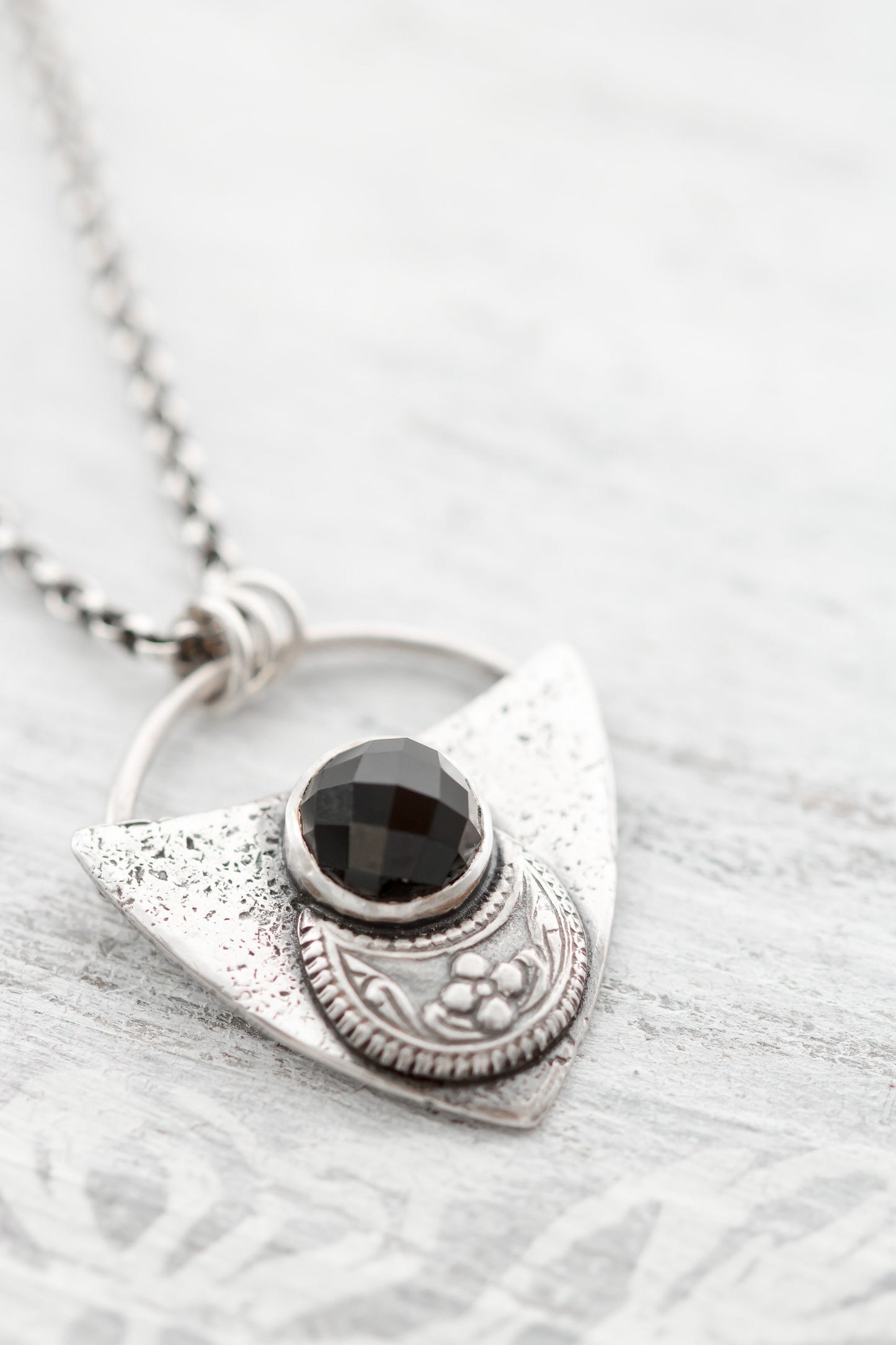 Shield shaped sterling silver pendant with floral patterned moon and faceted black onyx cabochon.