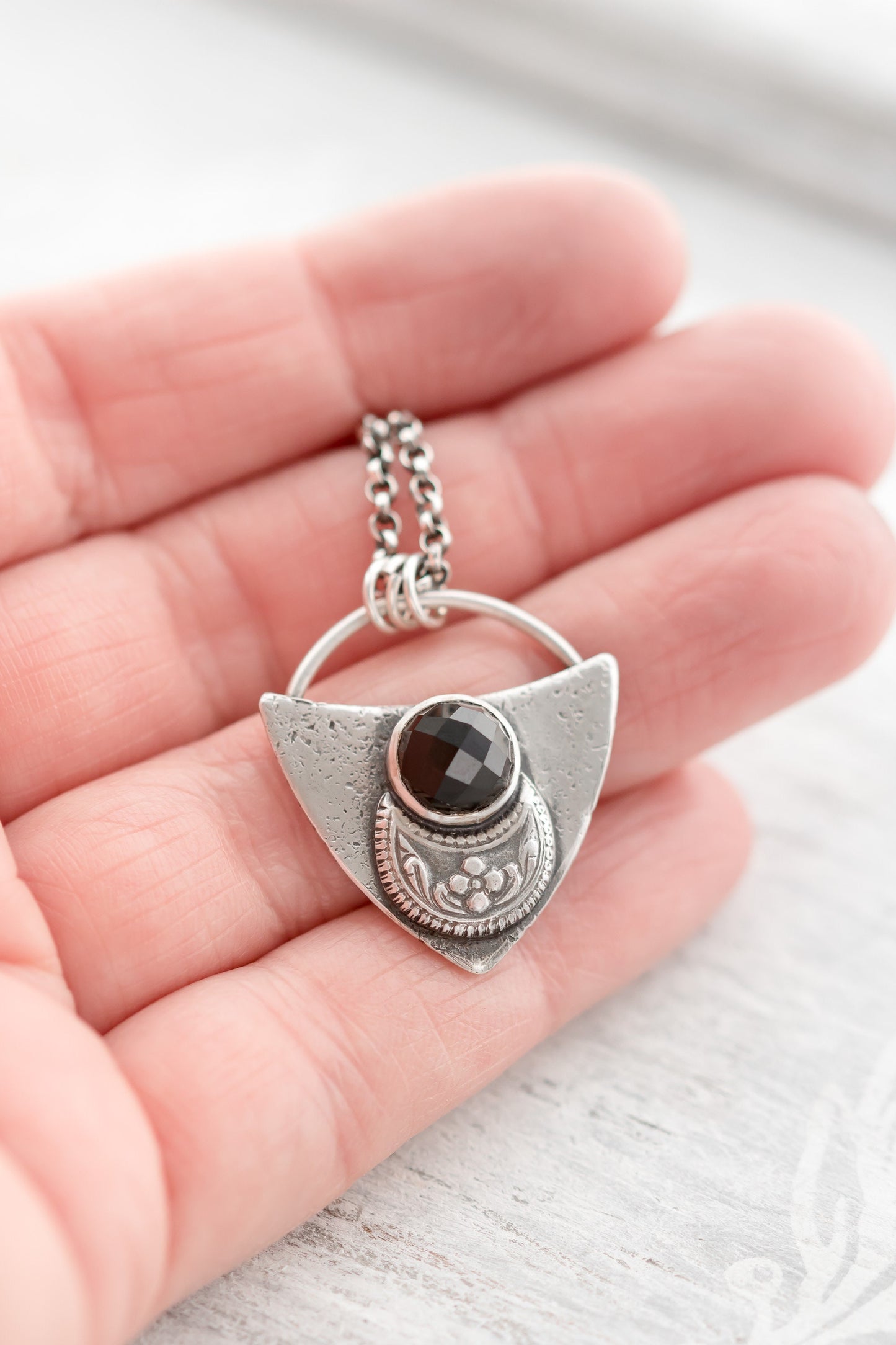 Shield shaped sterling silver pendant with floral patterned moon and faceted black onyx cabochon.