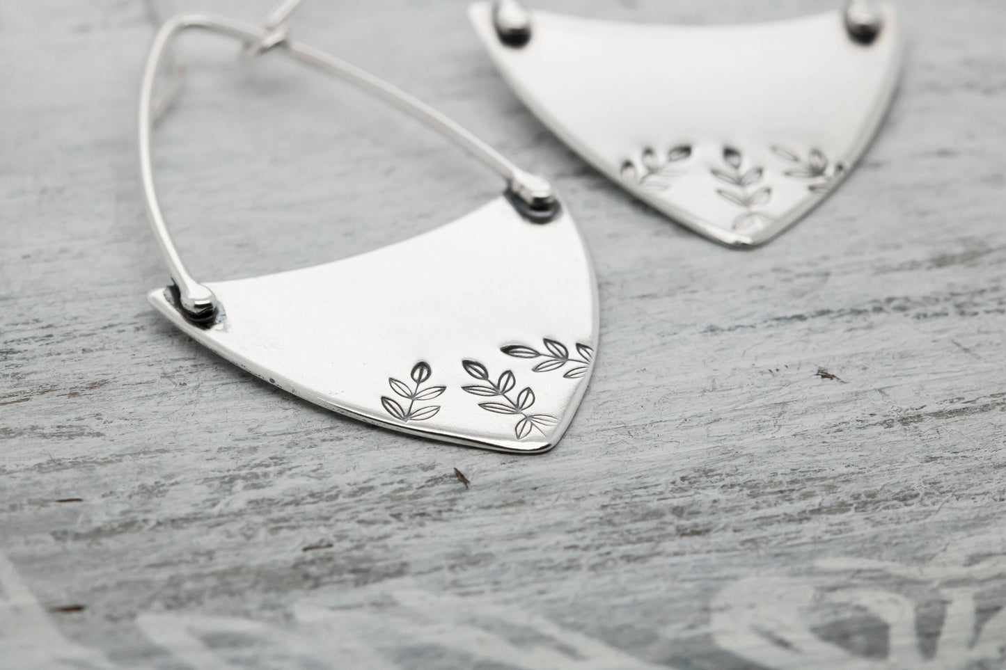 Handcrafted sterling silver fern-stamped hoop earrings on a wooden surface, showcasing elegant leaf designs.
