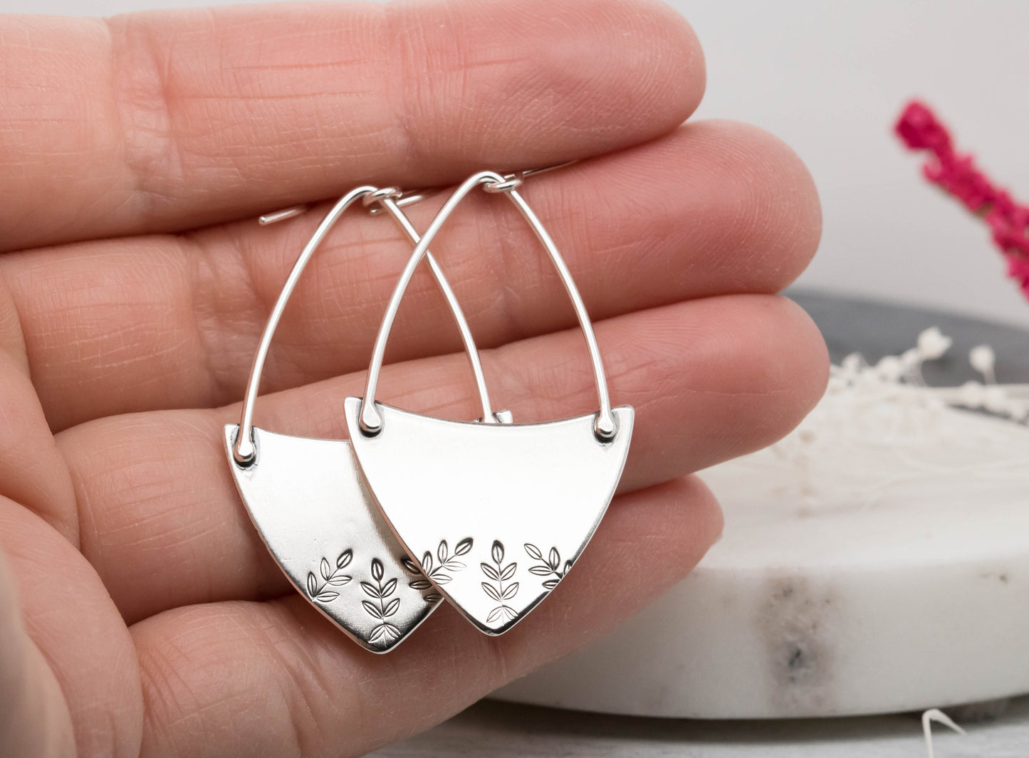 Handcrafted sterling silver fern-stamped hoop earrings held in a hand, showcasing elegant leaf designs.