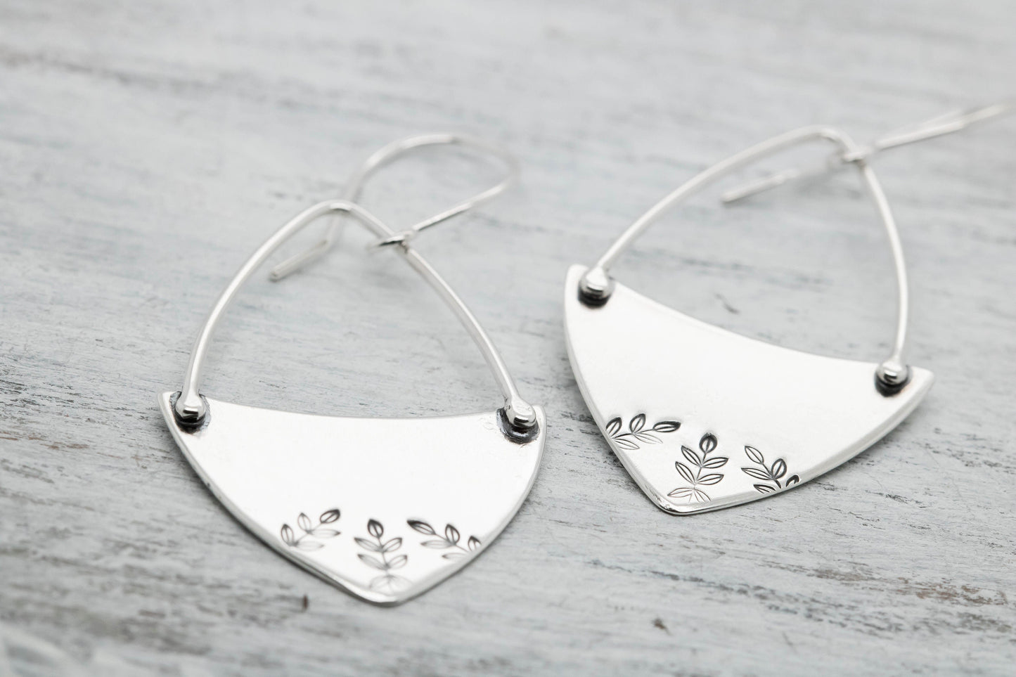 : Handcrafted sterling silver fern-stamped hoop earrings on a wooden surface, showcasing elegant leaf designs.