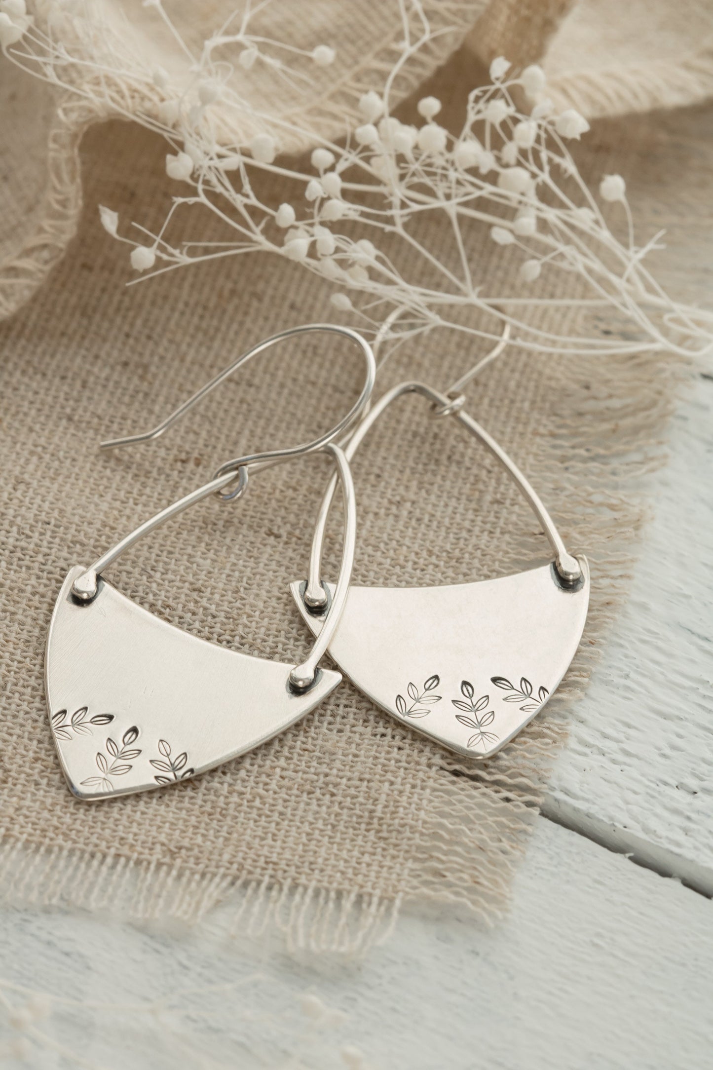 A pair of sterling silver hoop earrings with a floral fern design, displayed against a natural backdrop.