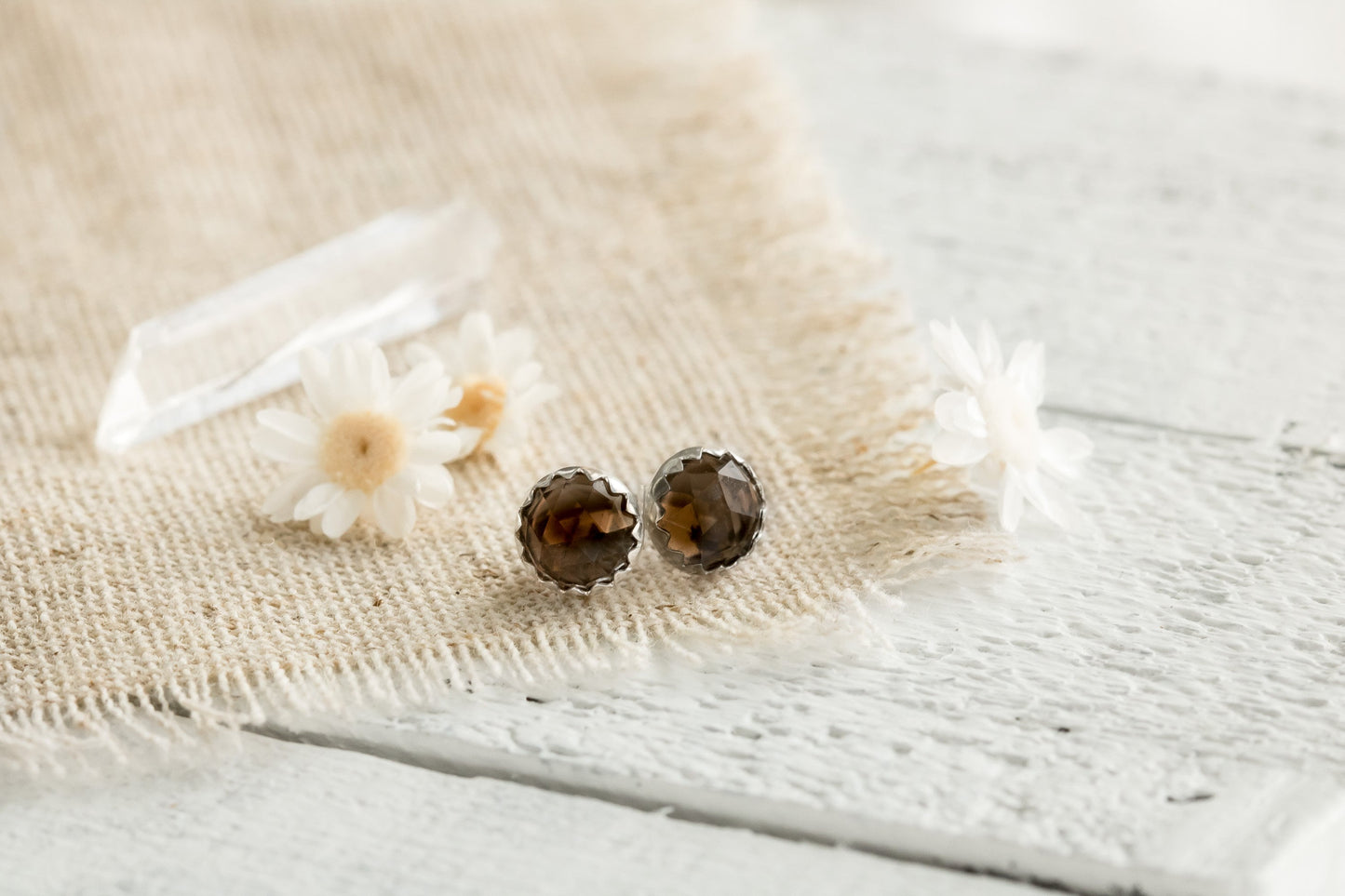 Smokey Quartz and sterling silver earrings on linen fabric with dried flowers and white wood background.