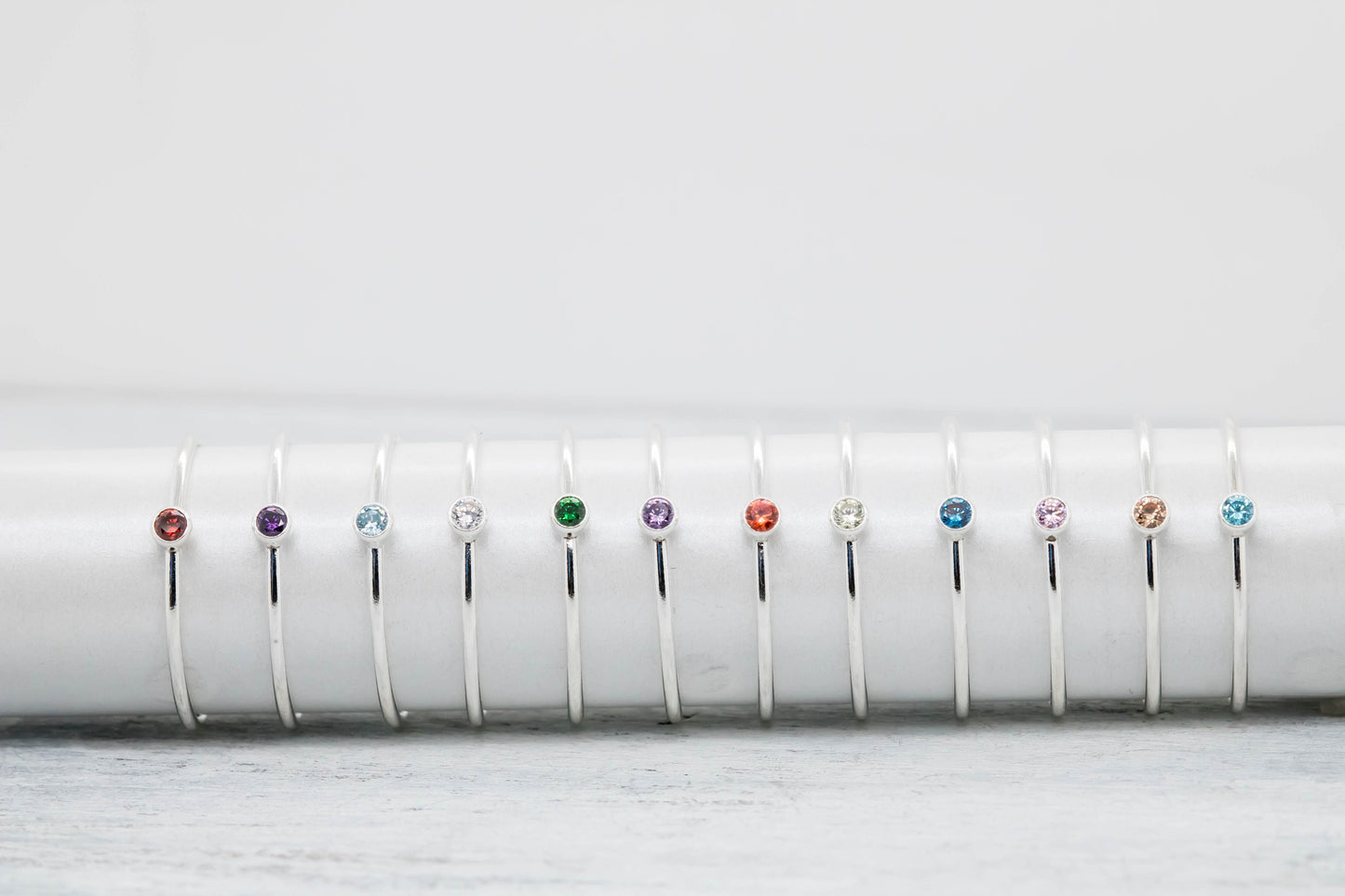 Sterling silver stacking rings with colorful cubic zirconia birthstones on a white stand, showcasing birthstone options.