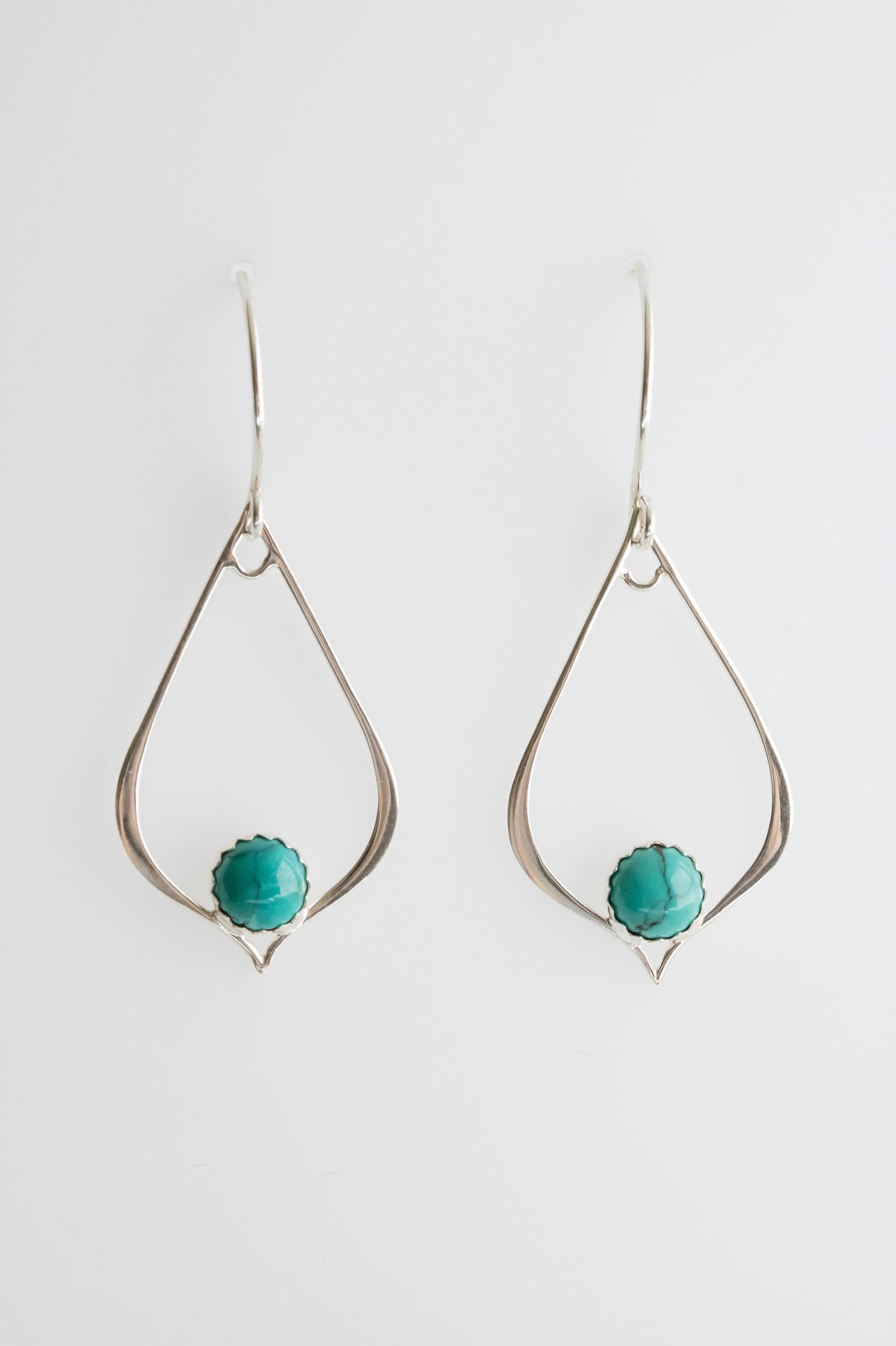 Two sterling silver teardrop-shaped earrings, each featuring a turquoise gemstone set in a detailed bezel on a white background.