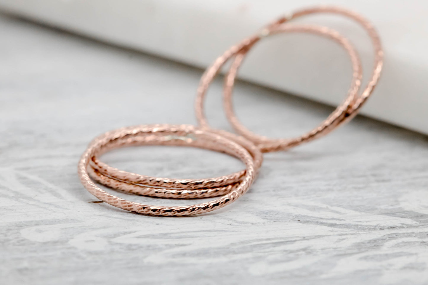 A stack of rose gold filled rings on a textured surface.