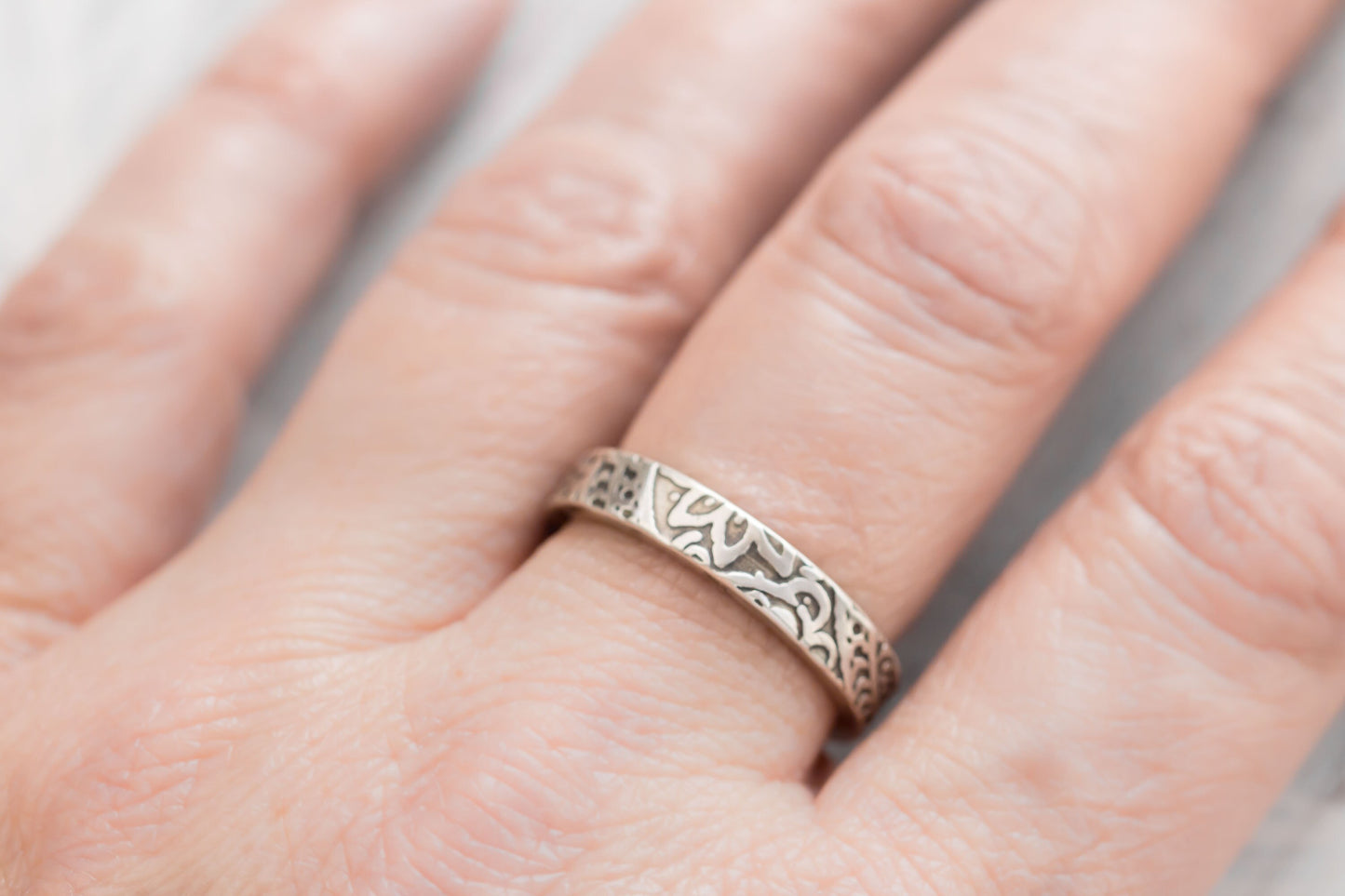 Close-up of a sterling silver floral textured ring on a finger, showcasing the intricate 4mm wide design against a blurred background.