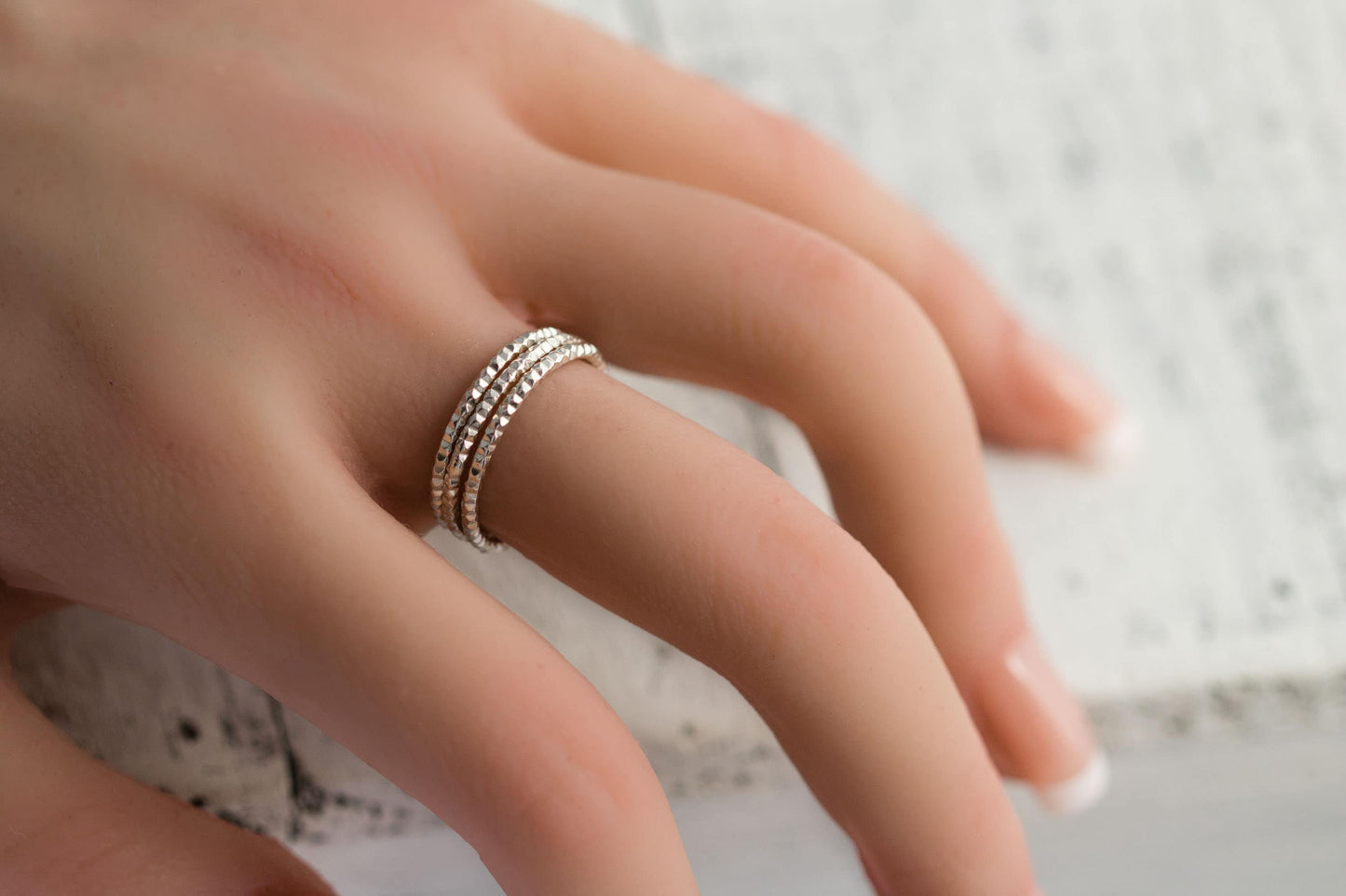 Hand with sterling silver diamond cut stackable rings, 1.5mm wide, minimalist style on rustic wood.