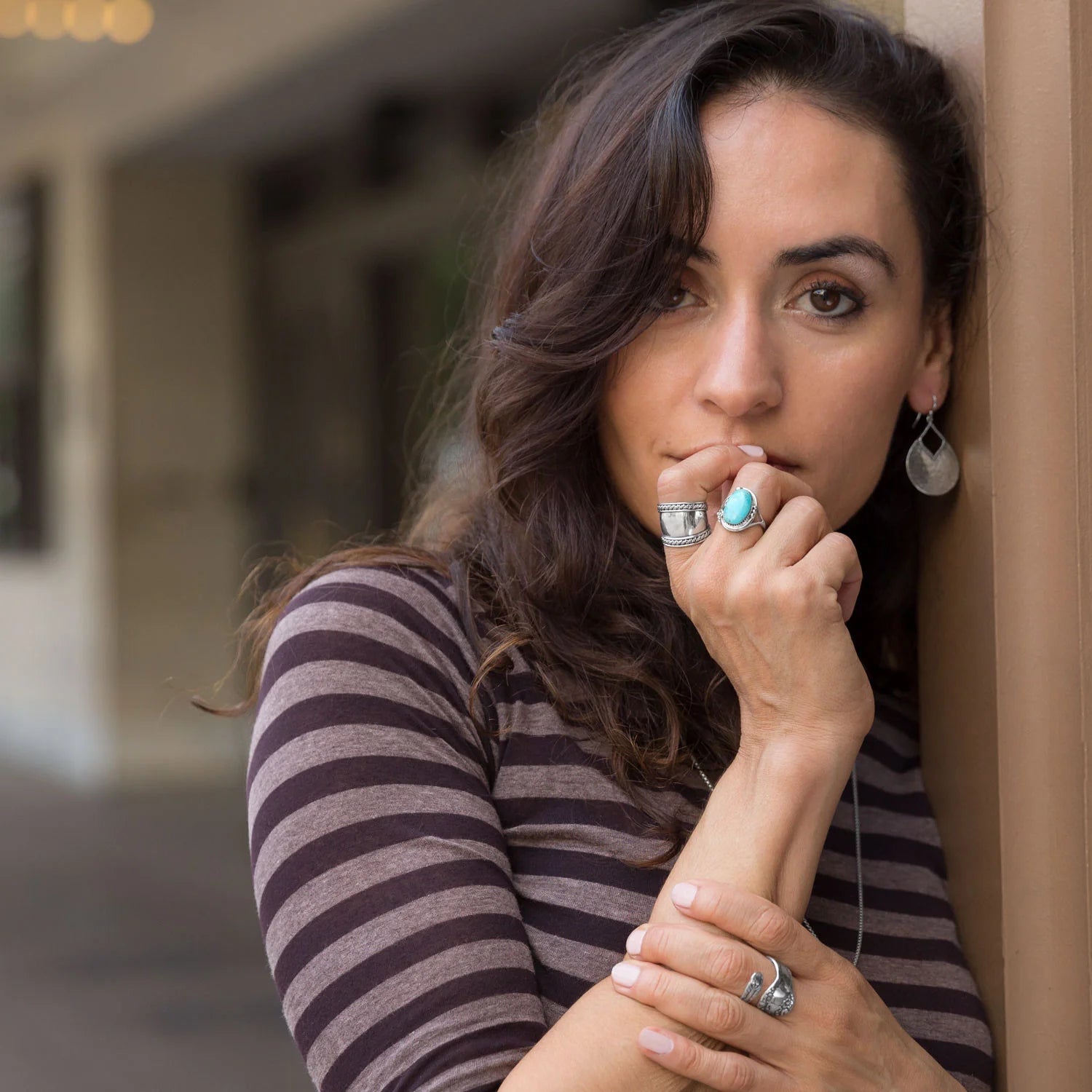 Woman with striped shirt and jewelry leaning against a wall