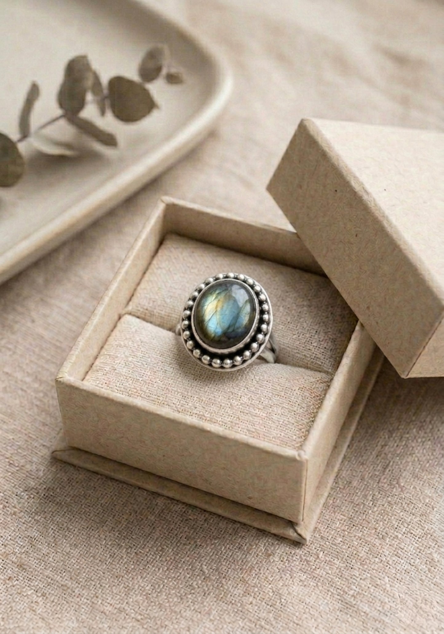 A sterling silver ring with a large, oval, iridescent labradorite gemstone. The gemstone is surrounded by a beaded border.