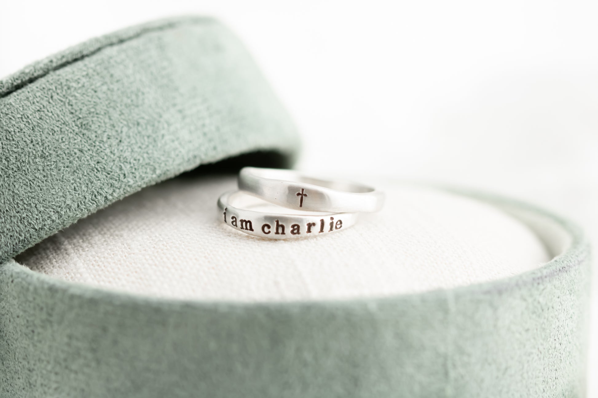 Silver ring with 'iam charlie' engraving on a light green fabric background