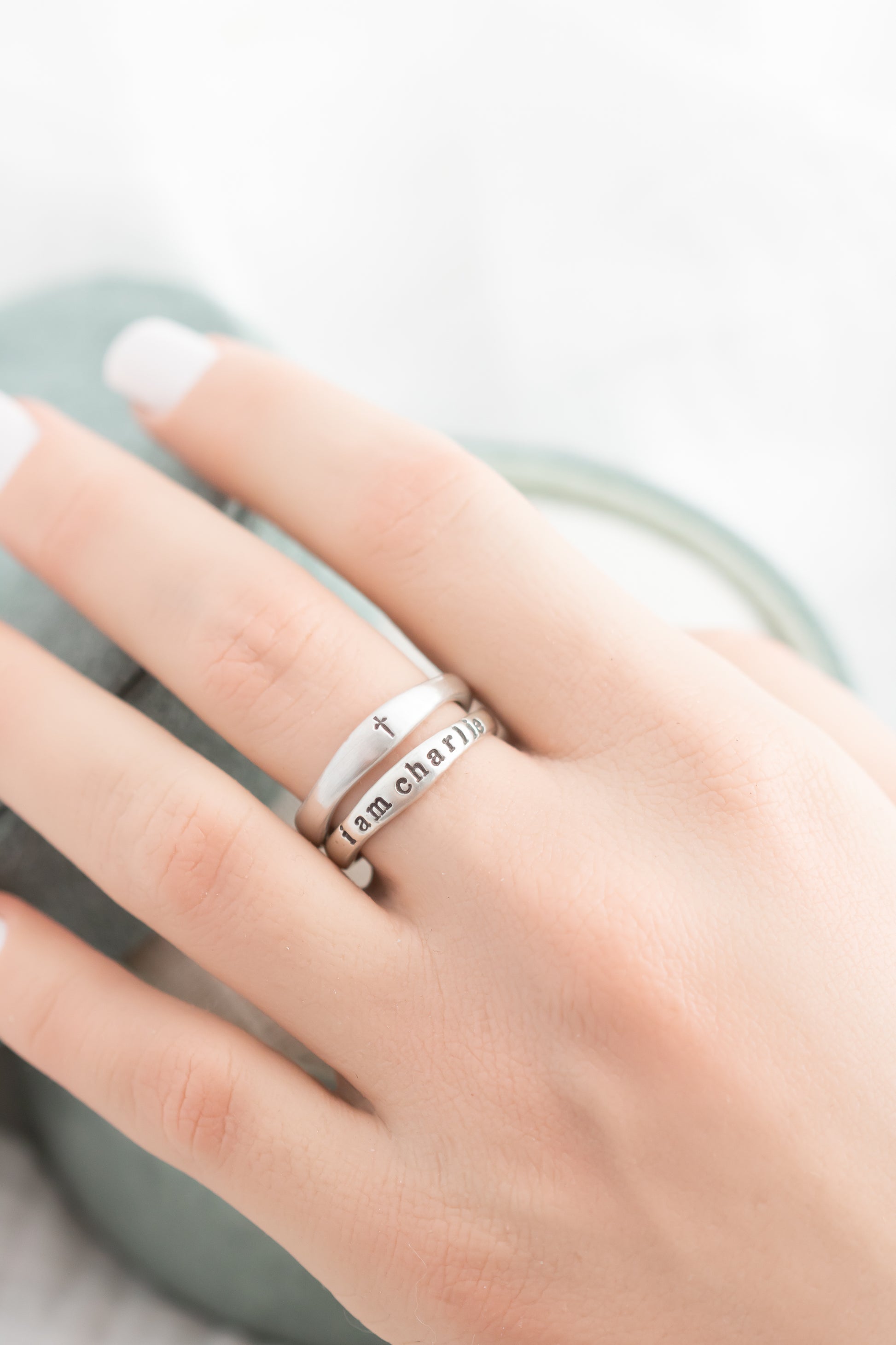 Hand wearing two silver rings with engraved text on a light background