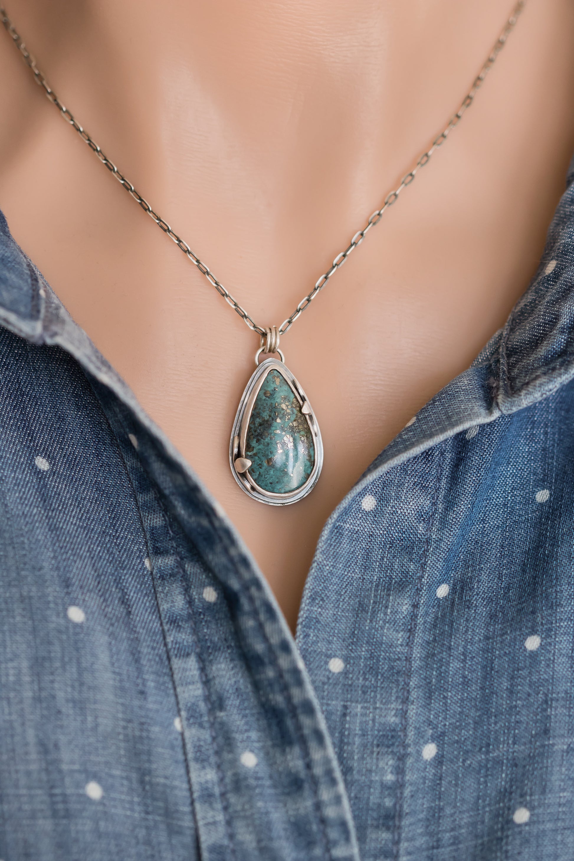 Handmade sterling silver Morenci 2 turquoise teardrop necklace worn on a model, styled with a blue polka dot denim shirt, highlighting the pendant's boho aesthetic.

