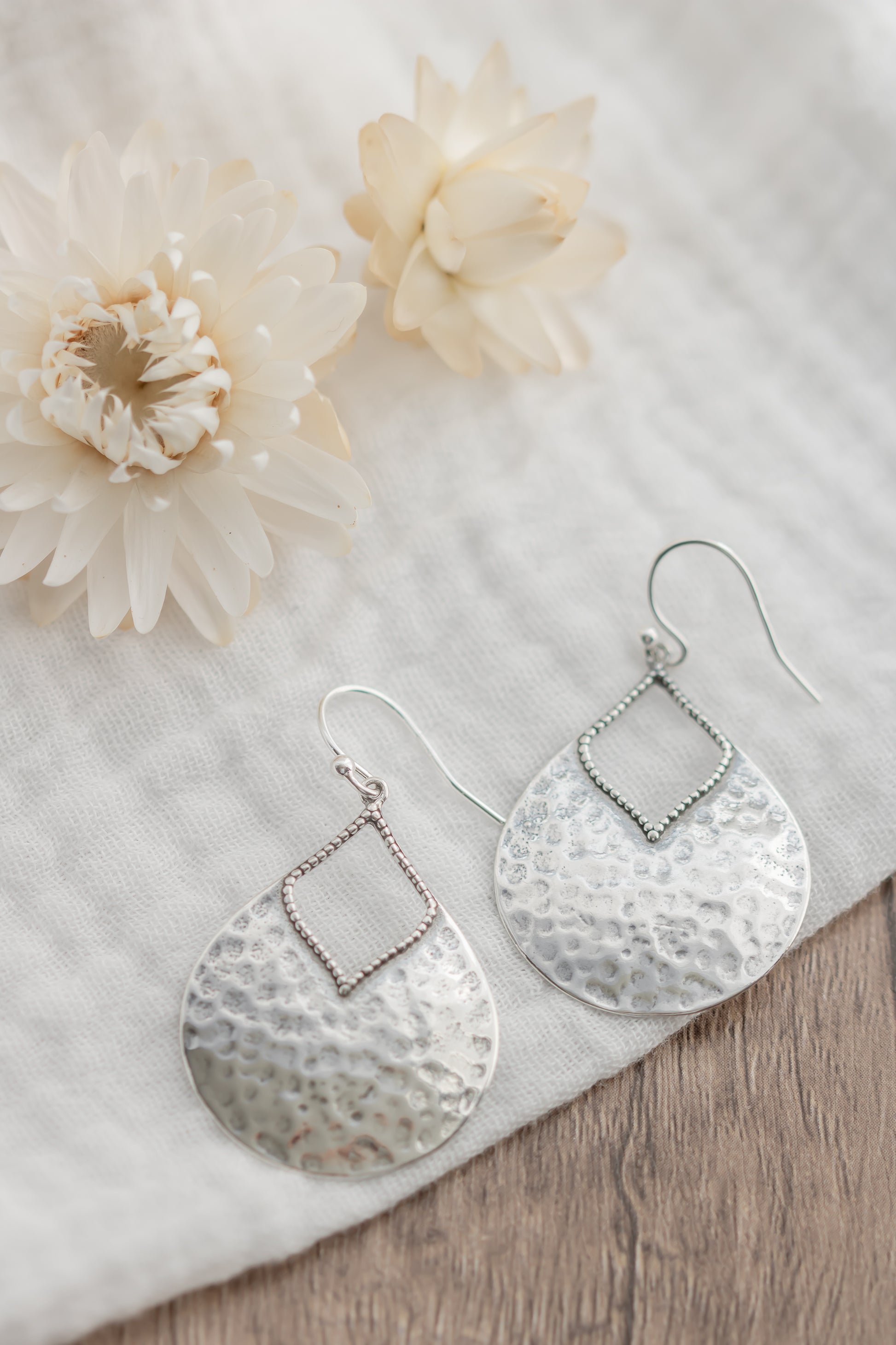Silver earrings on a white fabric background with flowers