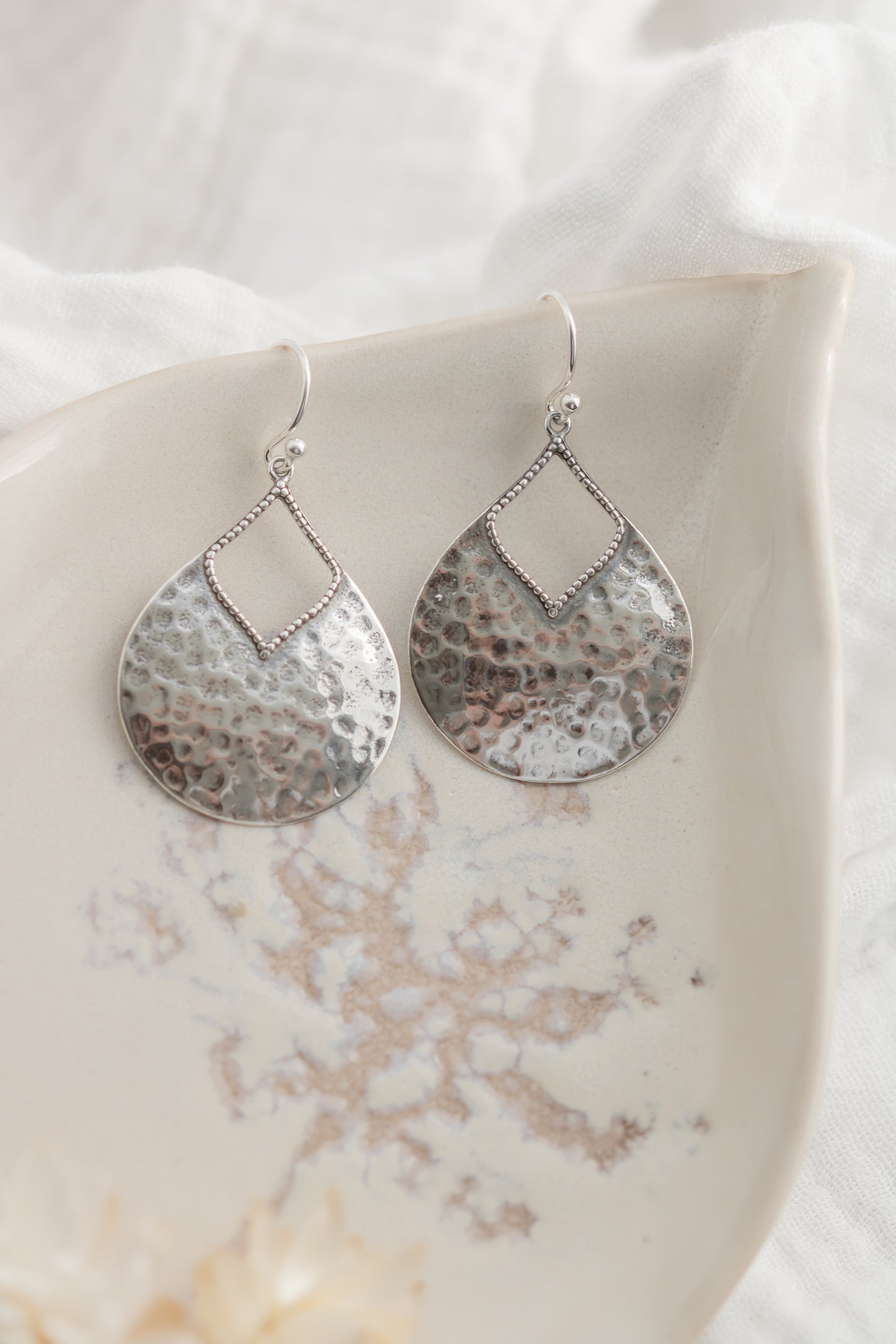 Pair of silver teardrop earrings on a marble surface