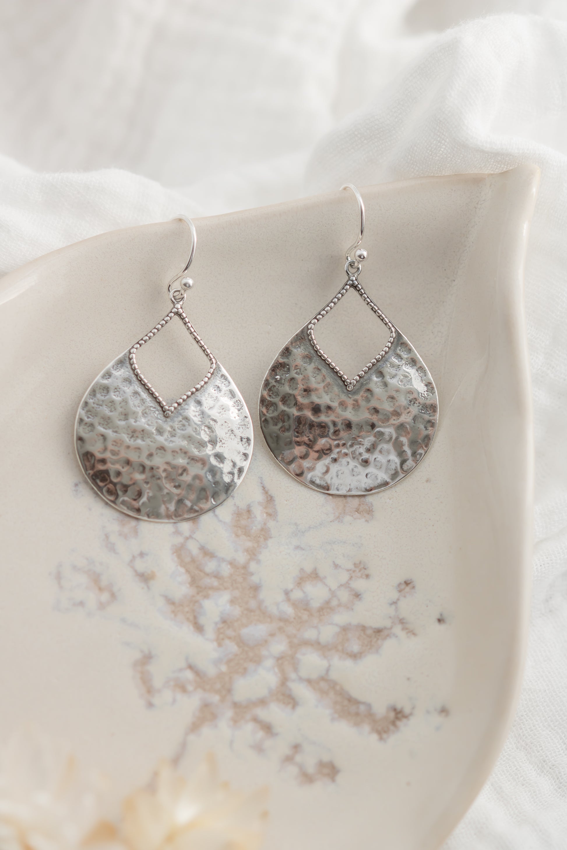 Pair of silver teardrop earrings on a marble surface