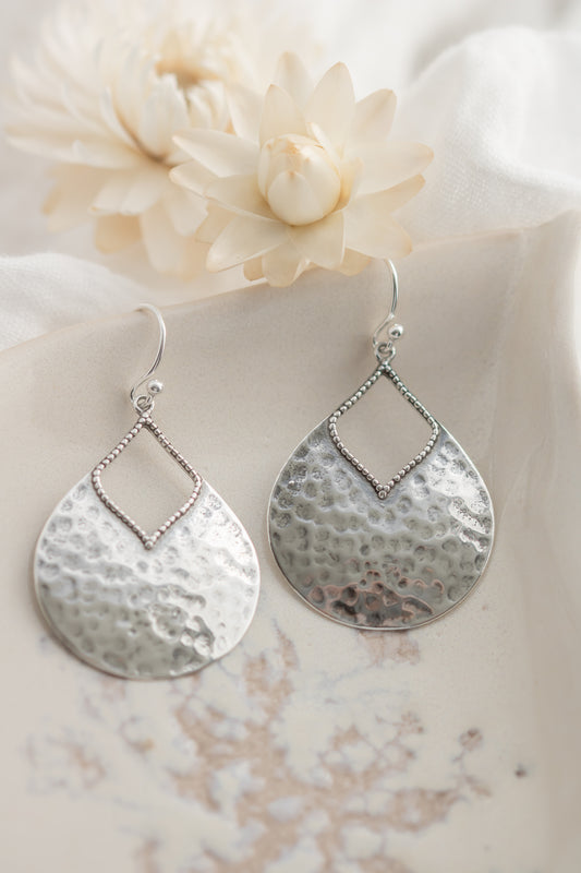 Silver earrings with a textured design on a soft fabric background
