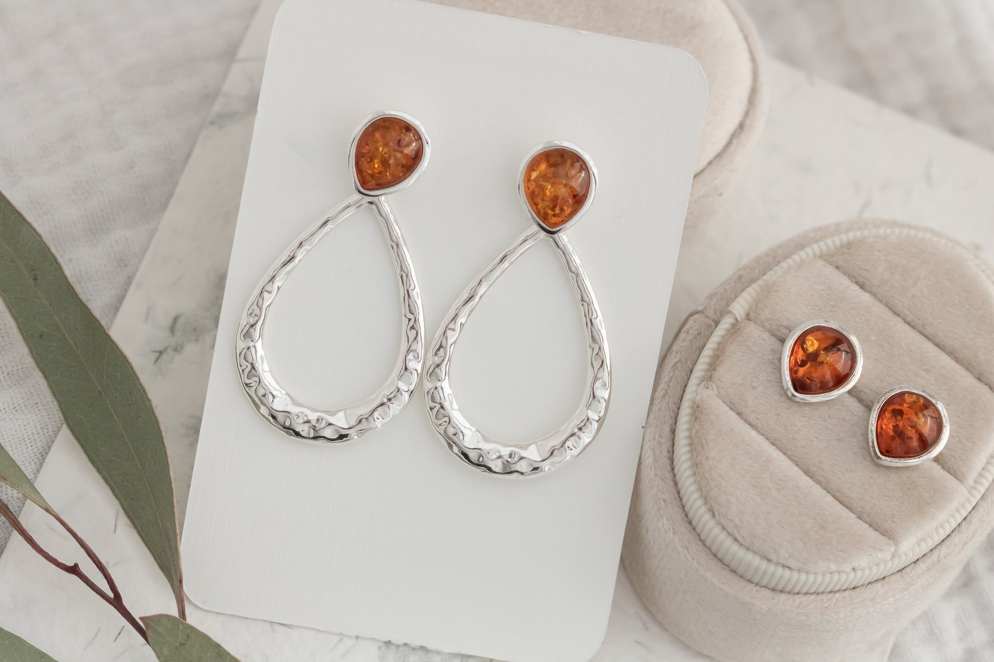 Pair of sterling silver hammered Baltic amber dangle earrings on white display card beside matching amber stud earrings  
