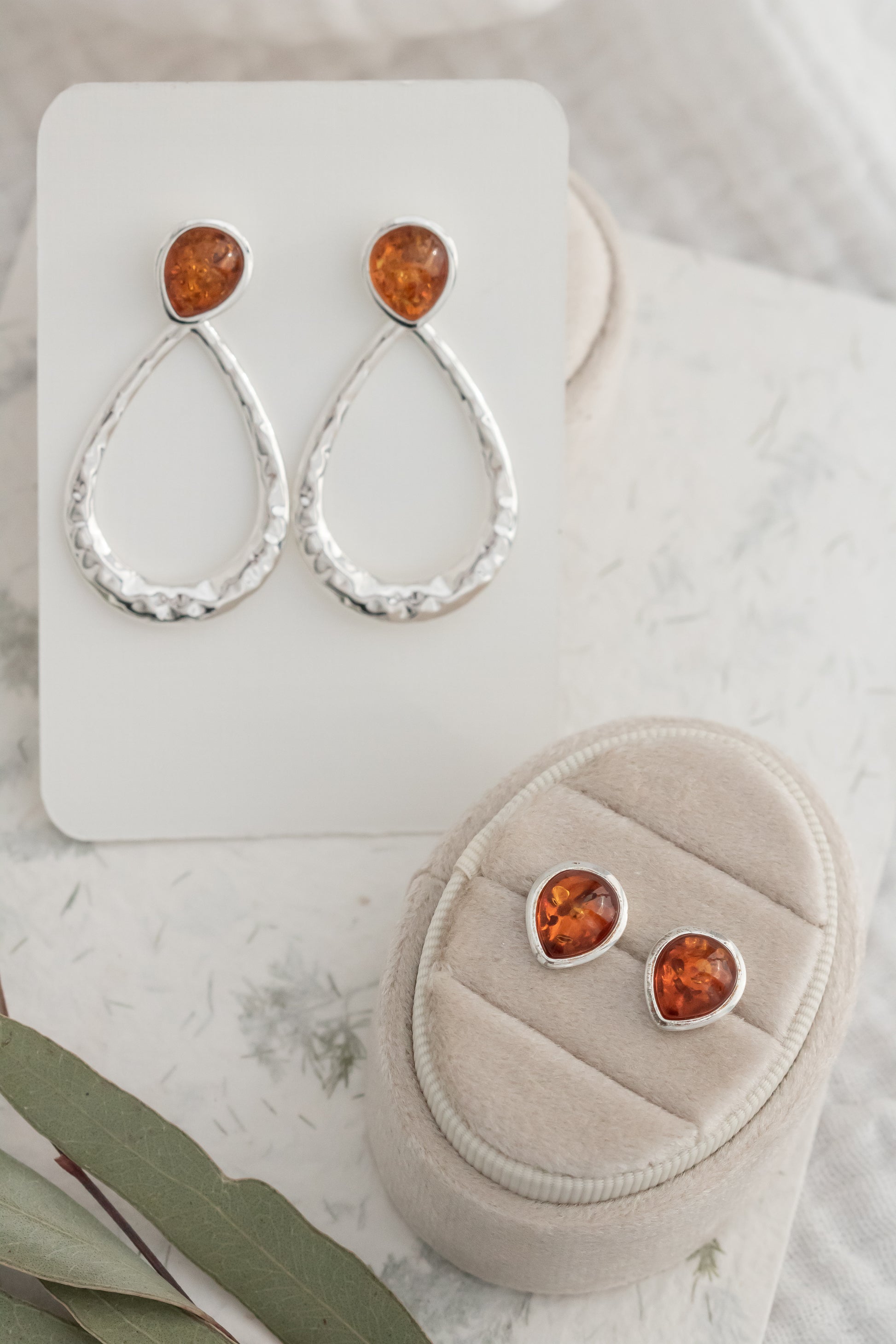 Pair of sterling silver hammered Baltic amber dangle earrings on white display card beside matching amber stud earrings  
