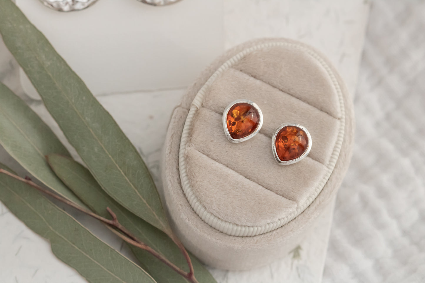  Close-up of genuine Baltic amber teardrop stud earrings displayed on beige velvet jewelry box  
