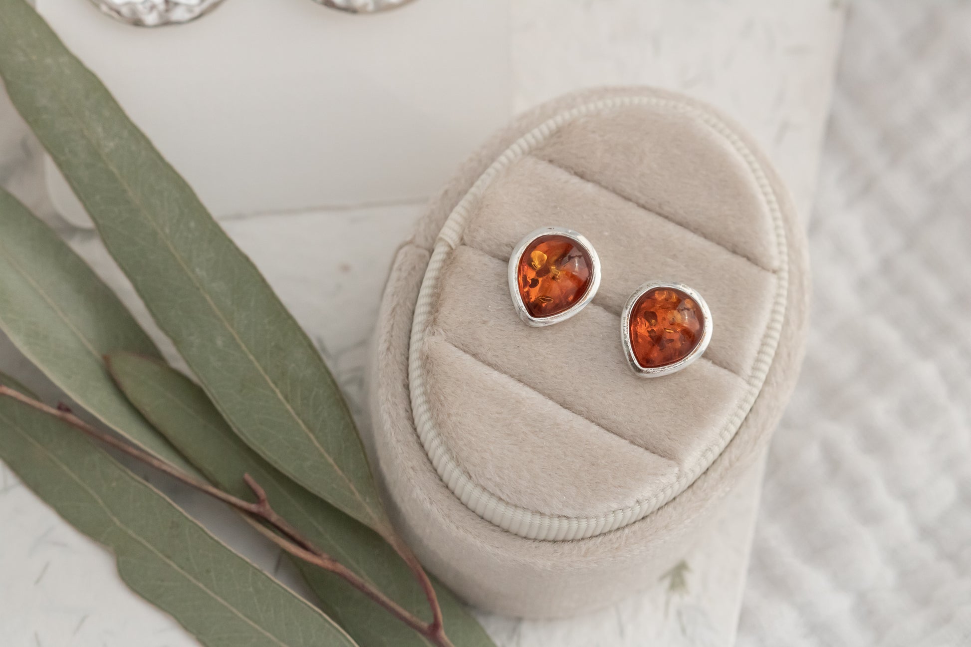  Close-up of genuine Baltic amber teardrop stud earrings displayed on beige velvet jewelry box  
