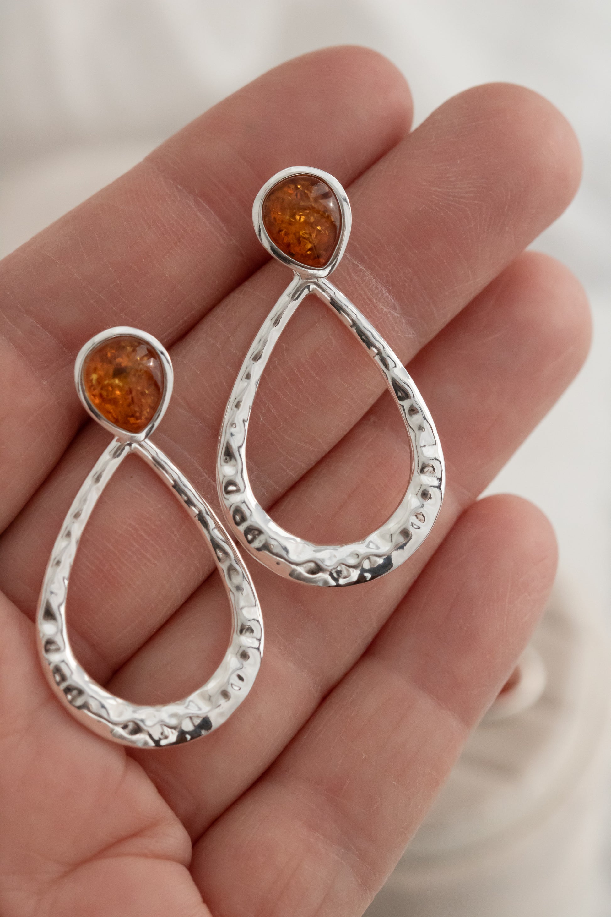 Silver earrings with amber stones held in a hand against a neutral background