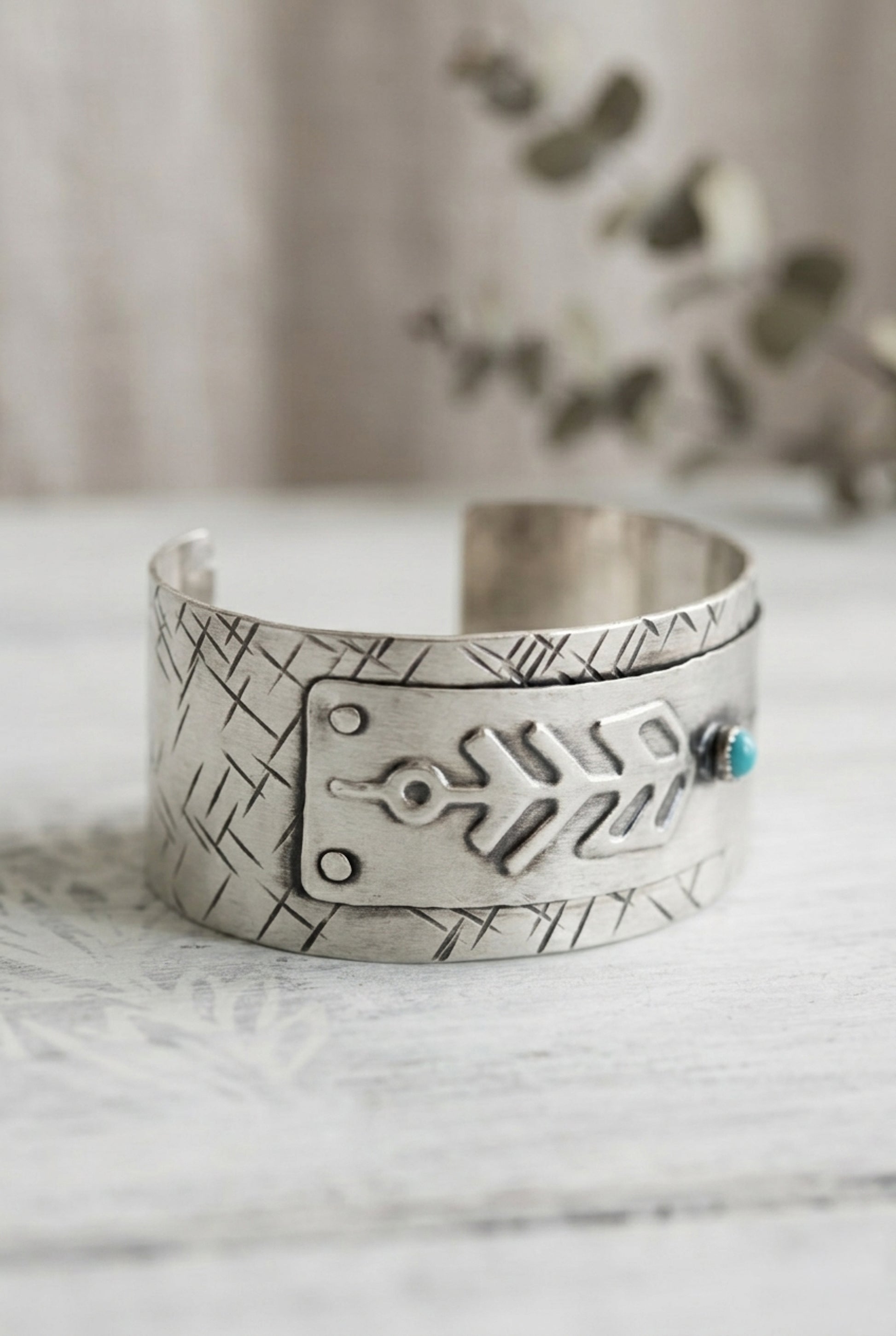 A sterling silver cuff bracelet with an arrow design and turquoise stone on a marble surface