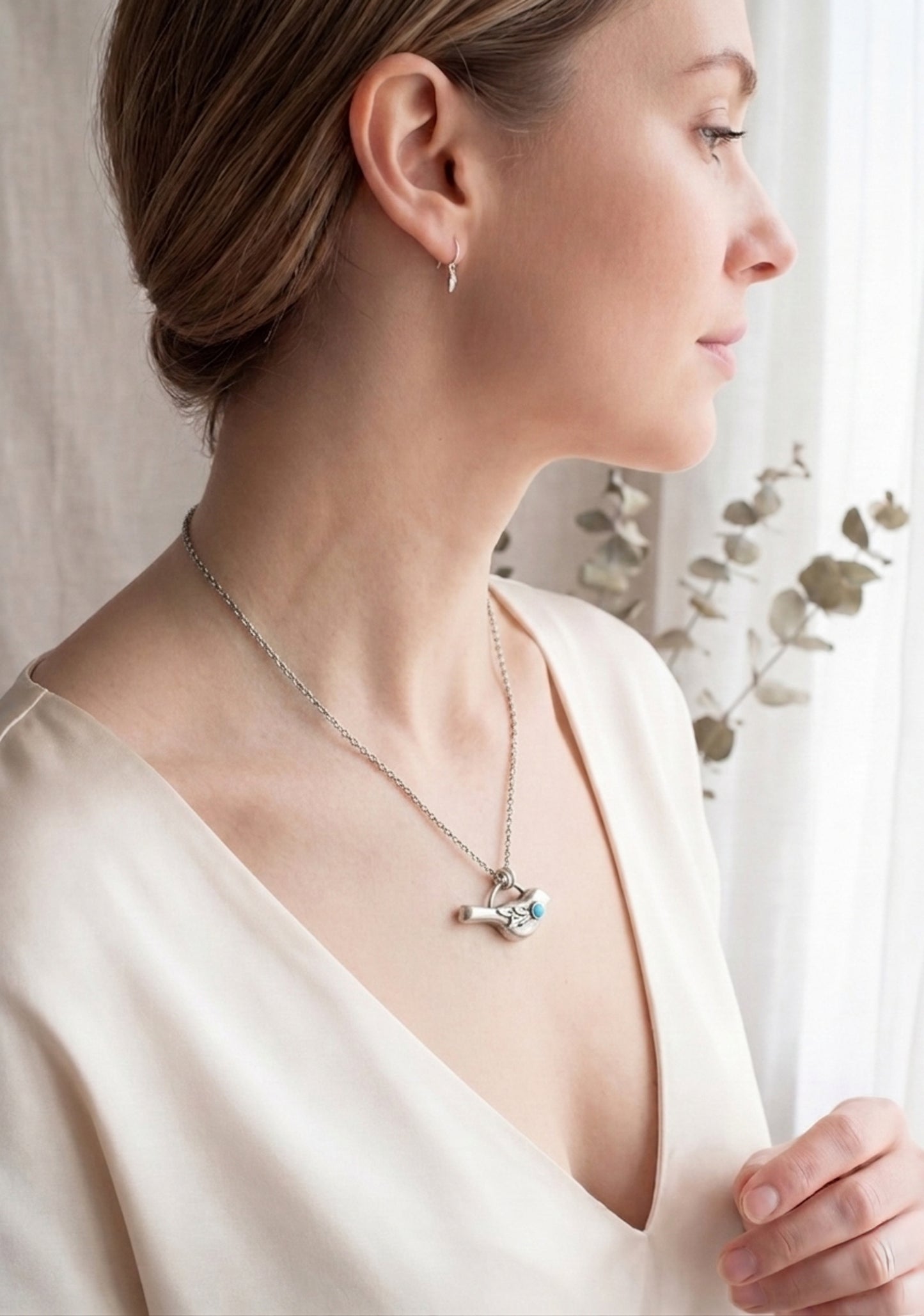 Woman wearing a sterling silver necklace with a bird pendant featuring a turquoise gemstone and a delicate leaf design. 