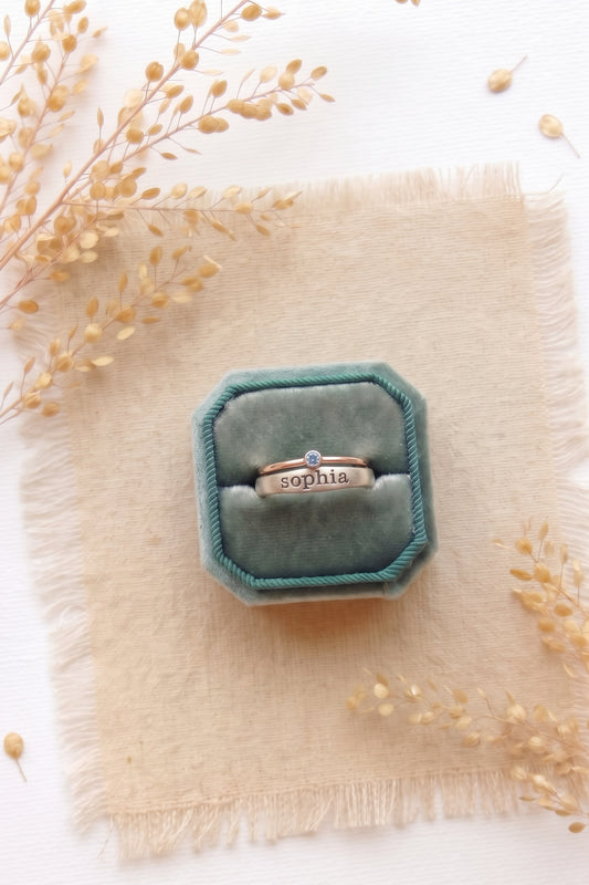 Sterling silver ring with the name Sophia and a sterling silver birthstone ring in a teal velvet ring box.
