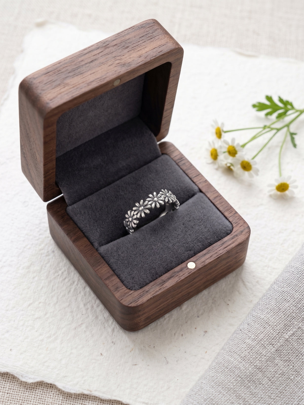 Oxidized 925 sterling silver daisy ring displayed in a dark velvet-lined wooden jewelry box beside fresh flowers.