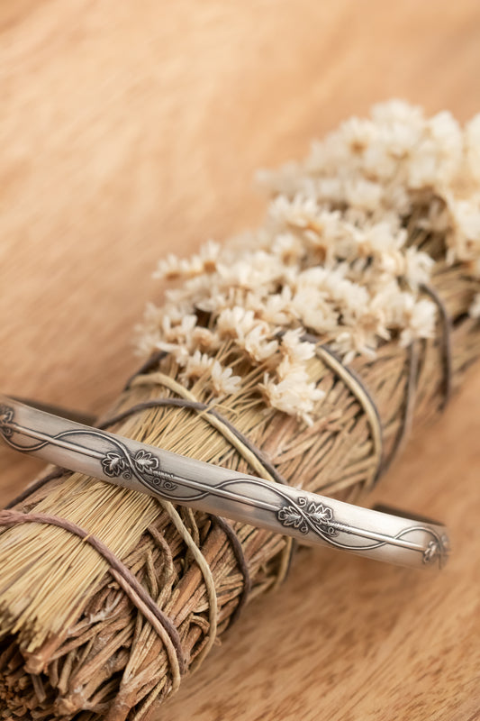Sterling silver bracelet with a floral vine design on a bundle of dried flowers and twine against a wooden background