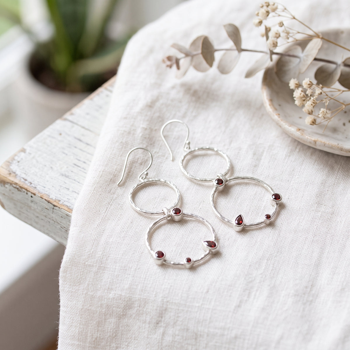 Garnet double-circle sterling silver drop earrings with hammered texture and French ear wires on cream fabric.